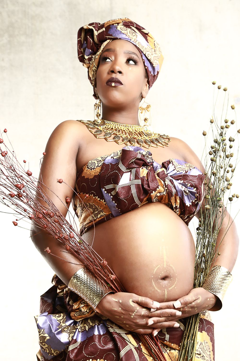 Maternity photoshoot featuring traditional African attire with dried flowers and golden accessories.