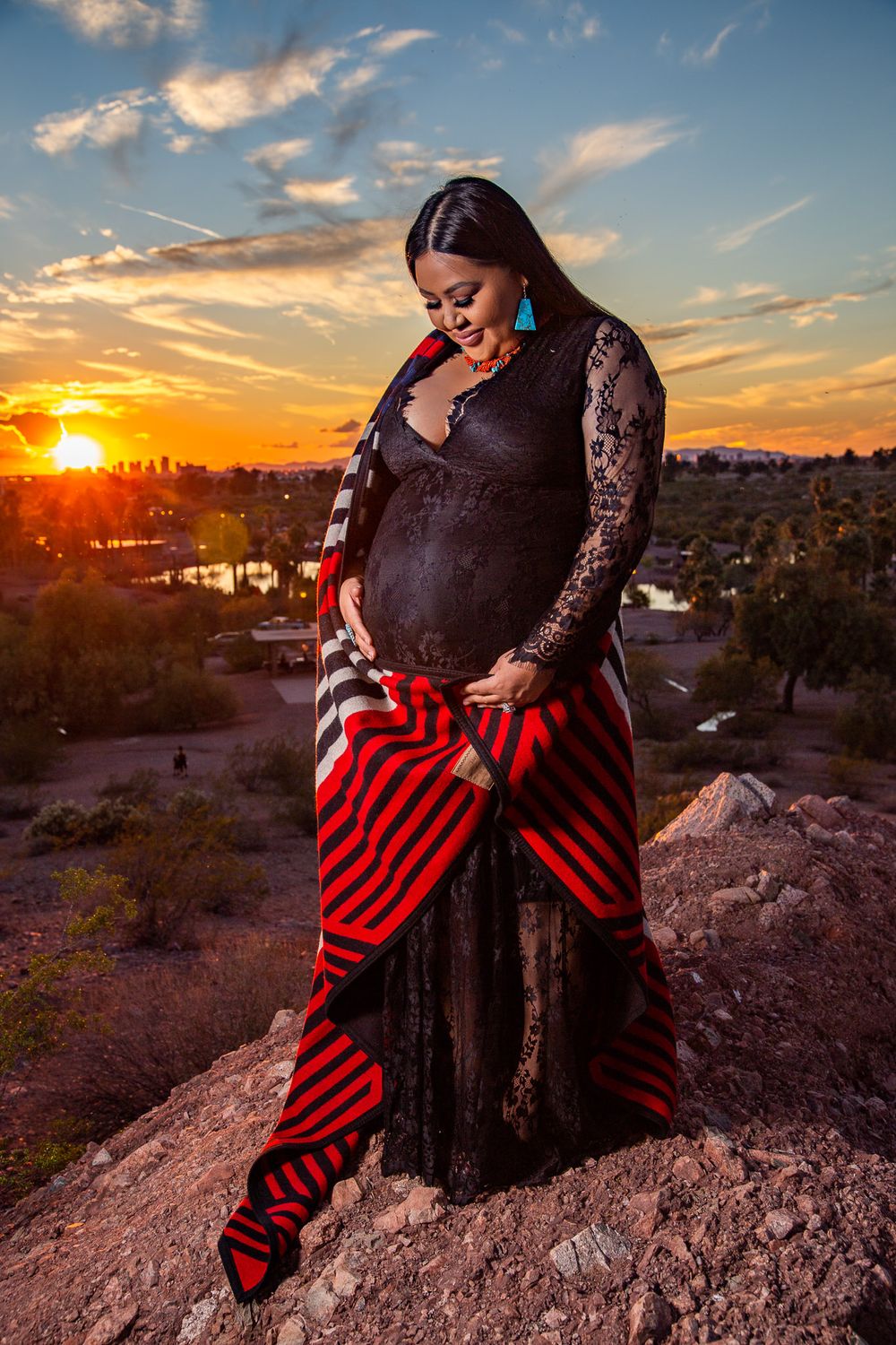 Maternity photoshoot at sunset featuring red and black striped pants against desert backdrop.