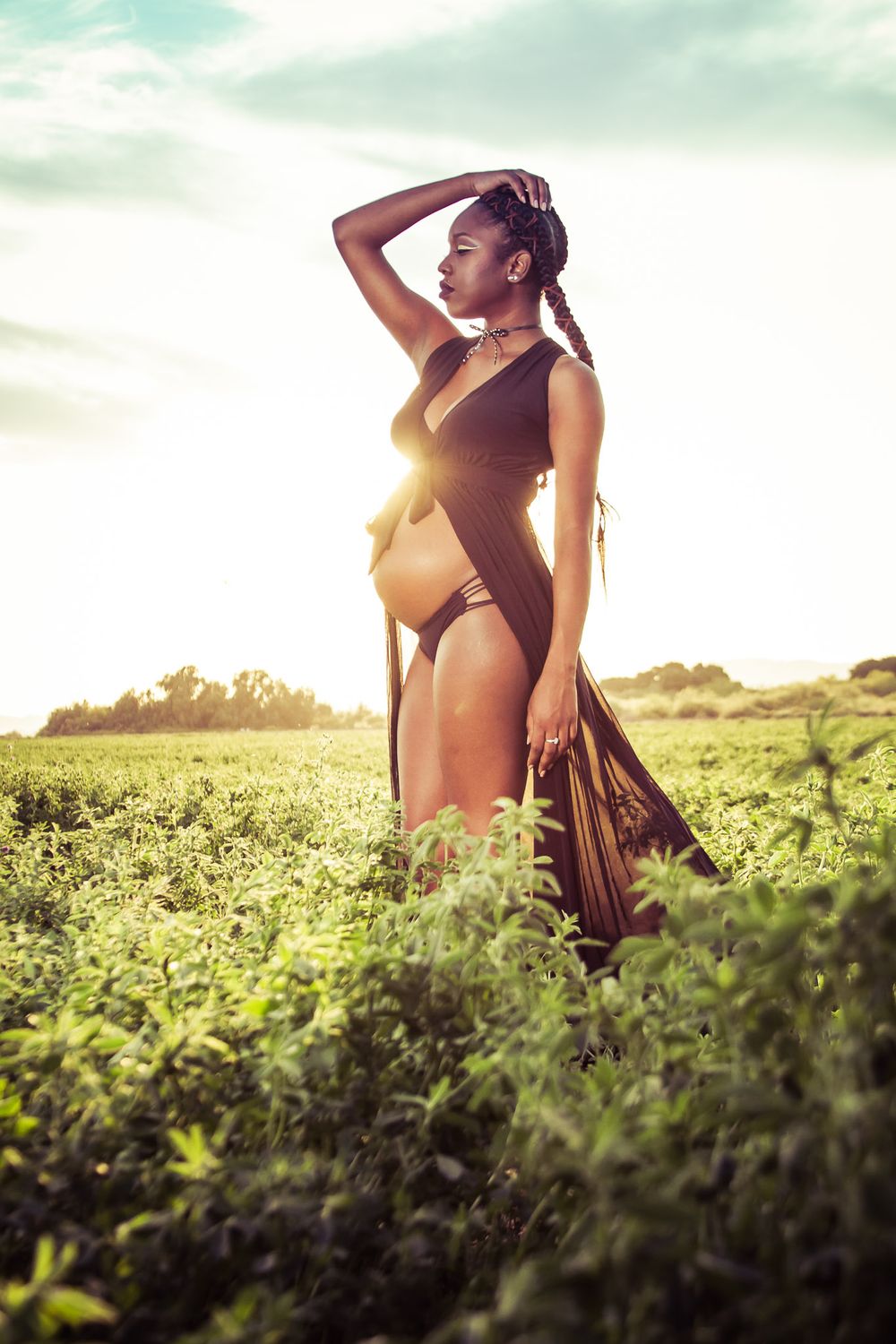 Silhouette figure in bikini poses against golden sunset in grassy field.