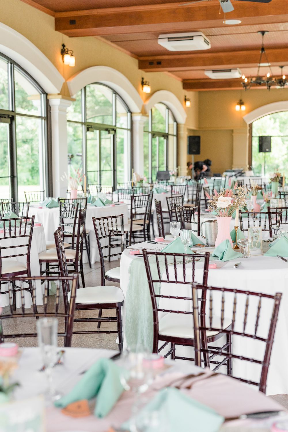 Reception venue with wooden beams, arched windows, and Chiavari chairs set for a wedding celebration.