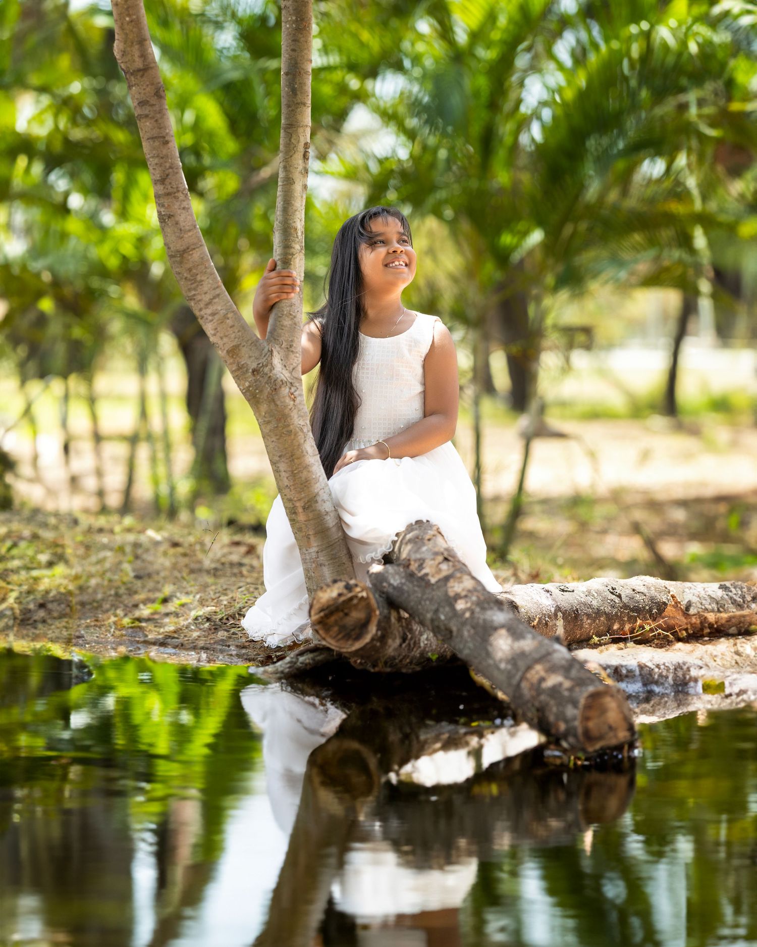 Peaceful outdoor portrait by a reflective pond with palm trees in the background.