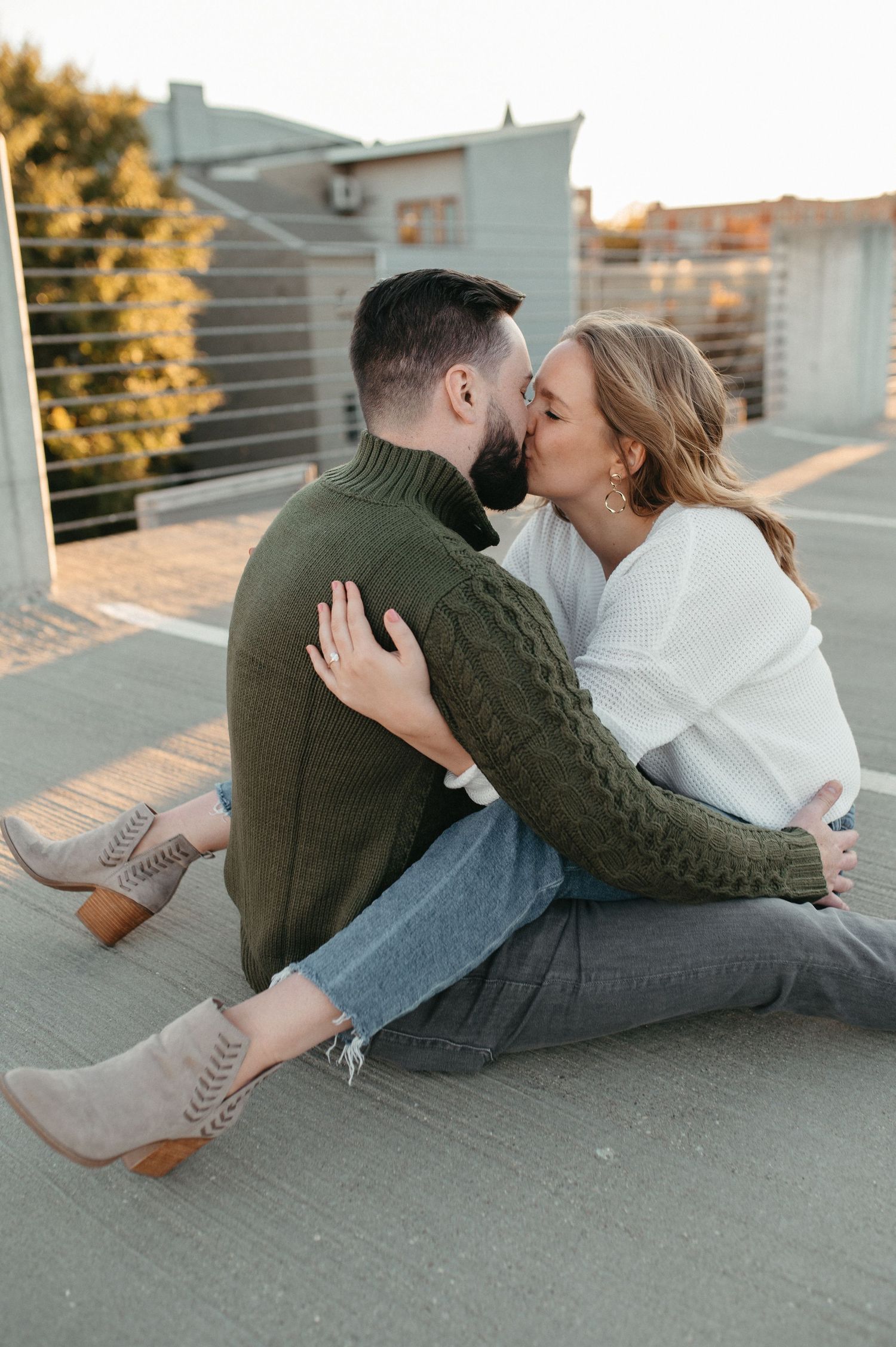 Couple embracing and kissing on a rooftop, wearing casual fall attire.