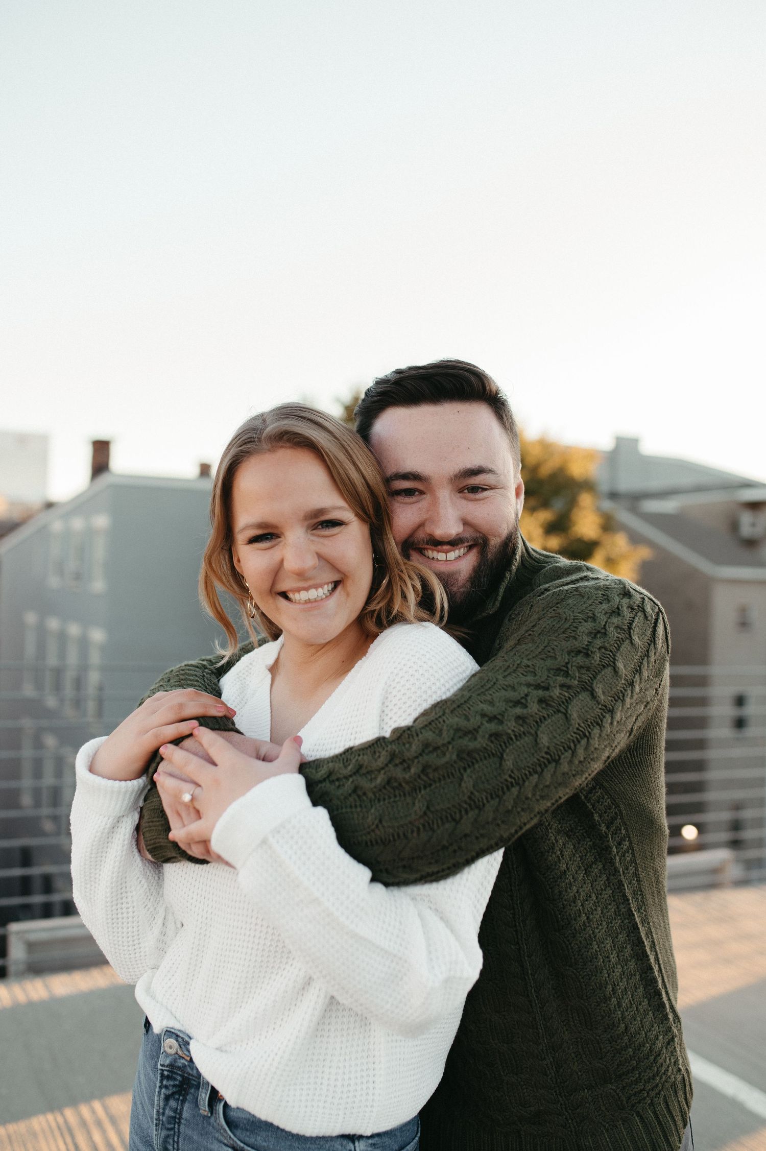 Happy couple embracing and smiling on a rooftop with city buildings in background.
