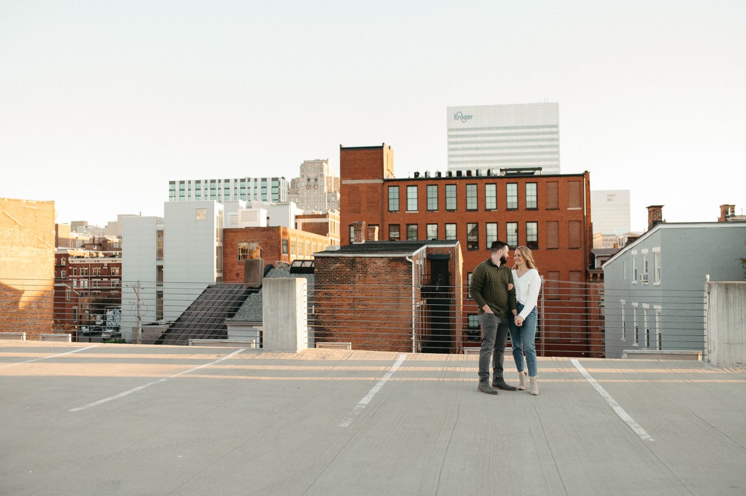 Two people share an intimate moment against an urban backdrop of brick buildings and sky.