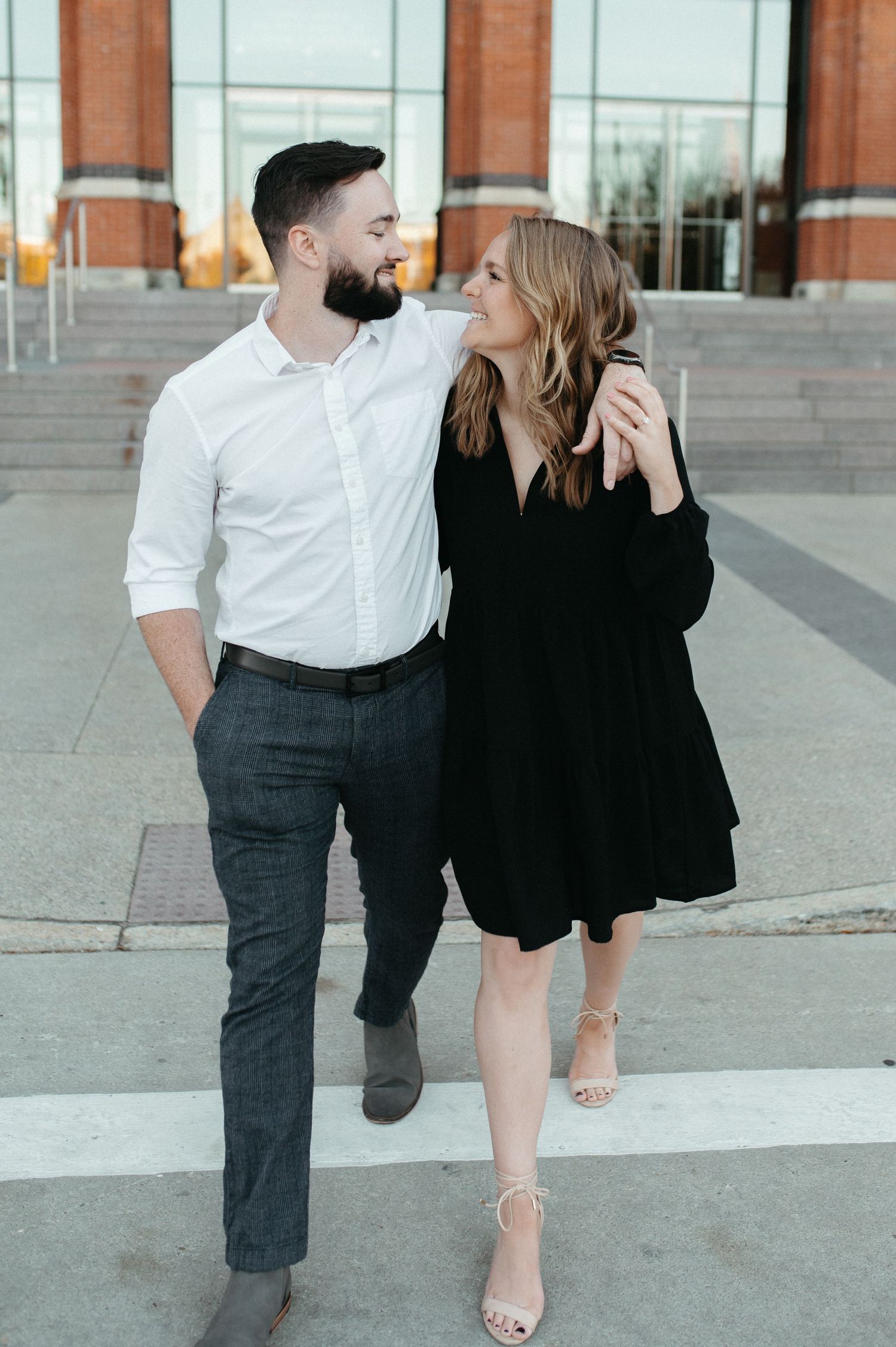 A couple in contrasting black and white outfits poses together on city steps.