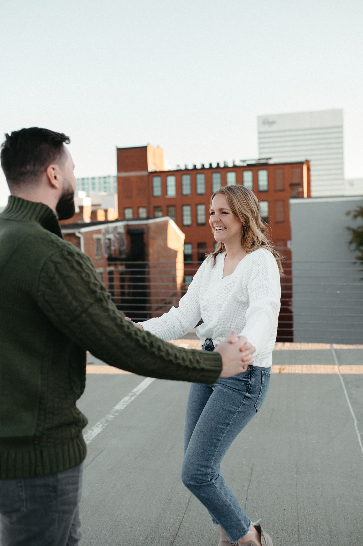 A happy couple dancing and holding hands on an urban rooftop with buildings in background.