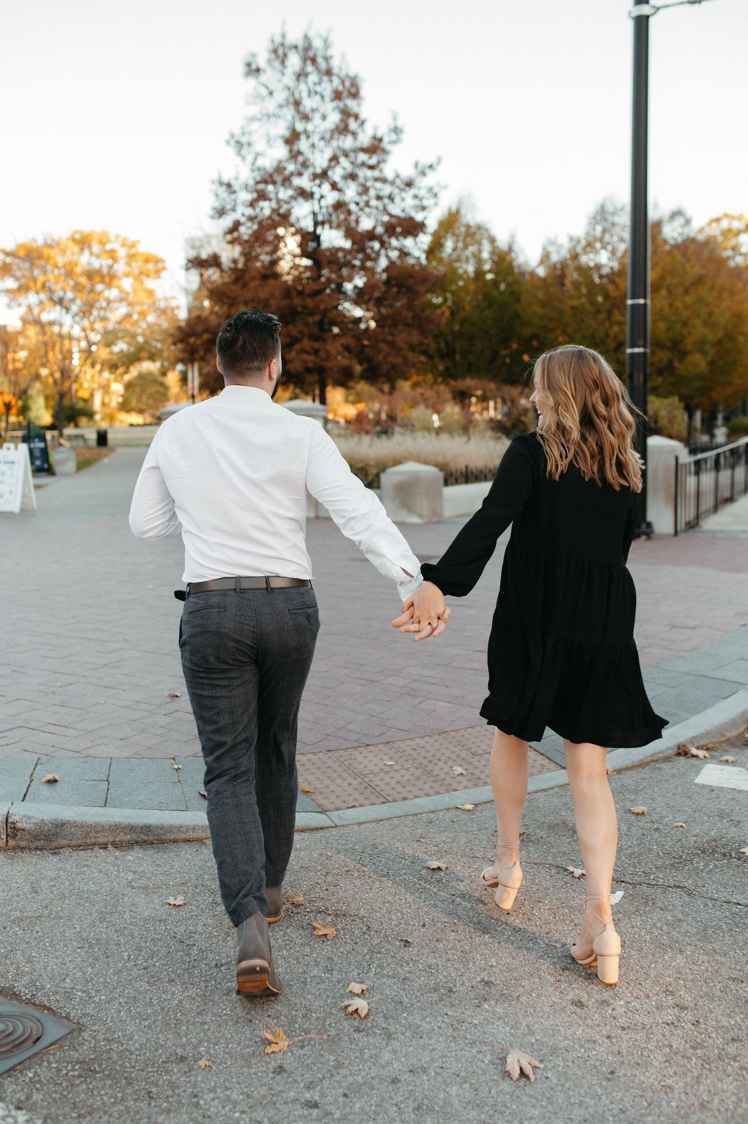 A couple walking hand in hand on a brick pathway during fall season.