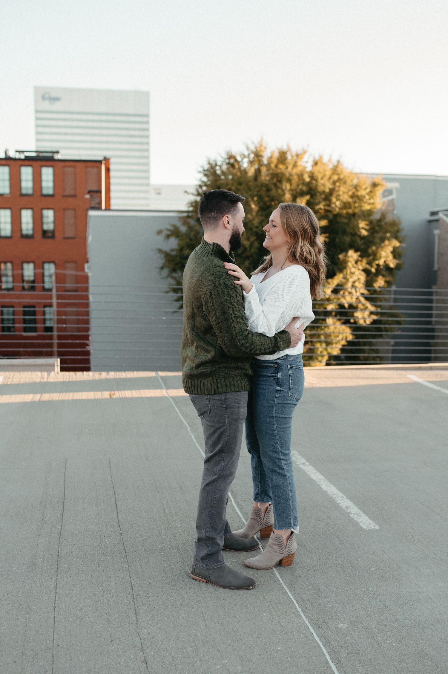 A couple embraces while standing together on an urban rooftop with city buildings in the background.