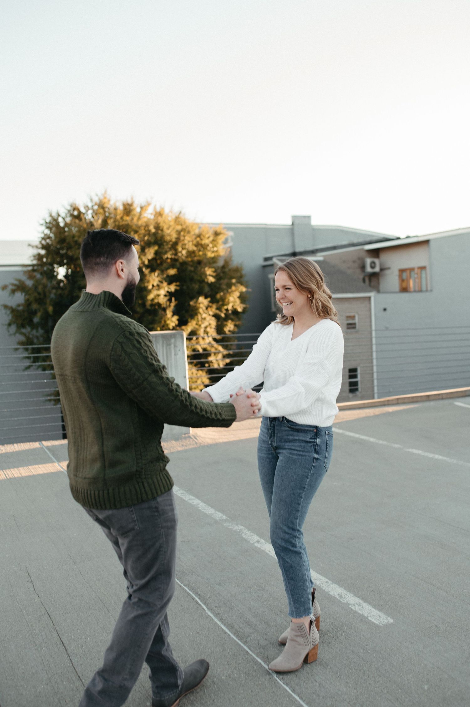 A couple dancing and laughing together on an urban rooftop at sunset.