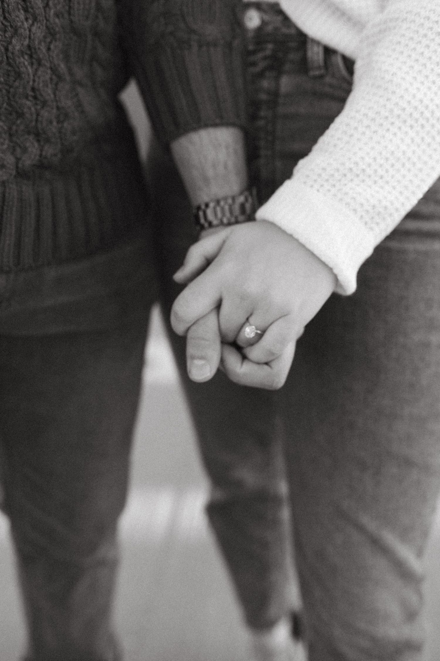 Black and white close-up of clasped hands showing an engagement ring.