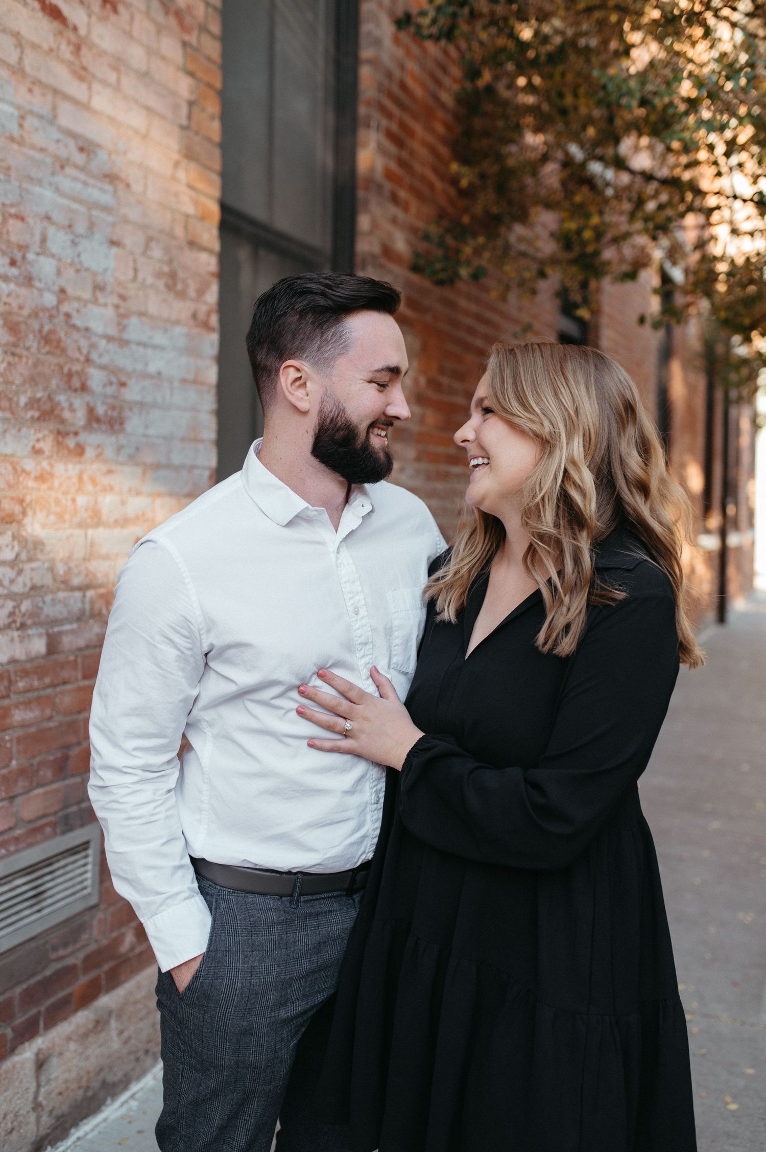 A couple sharing a romantic moment against a rustic brick wall with warm lighting.