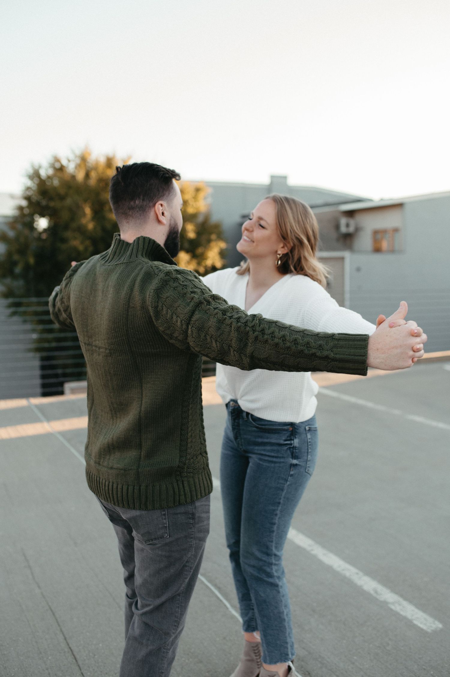 A couple dancing and smiling on a rooftop parking area at sunset.