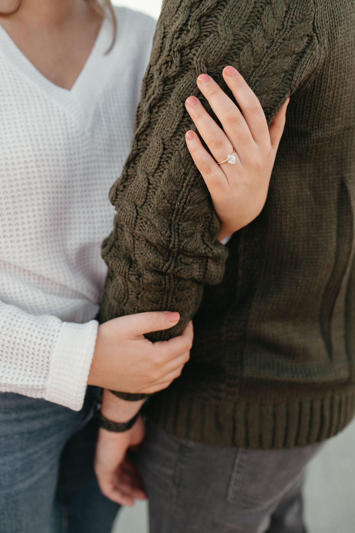Close-up of hands on a cable knit sweater showing an engagement ring.