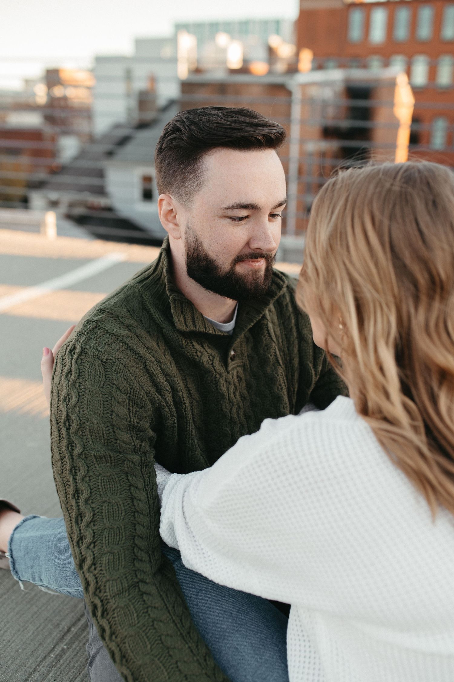 A couple in casual attire share an intimate moment during their rooftop photoshoot.