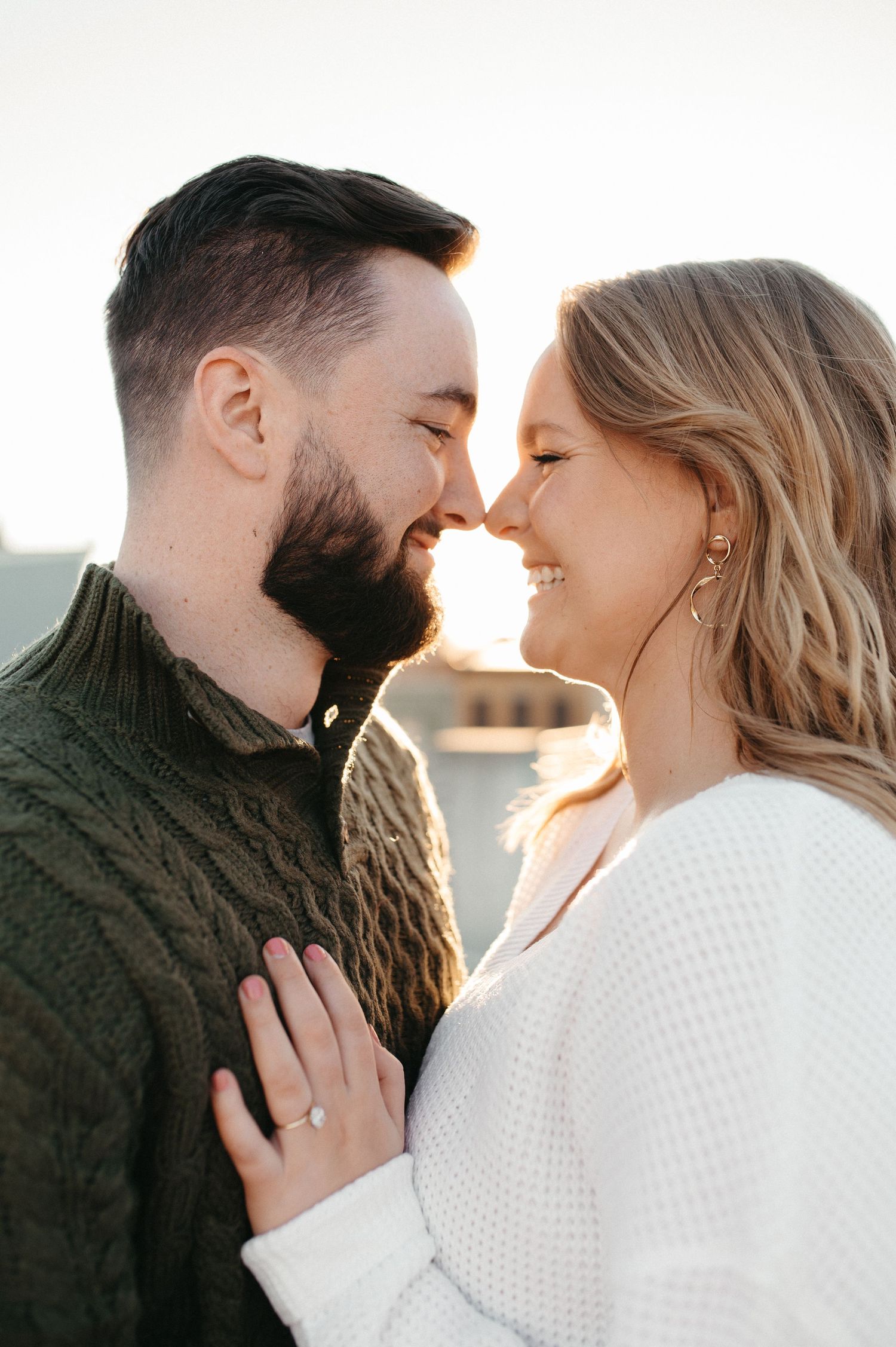 Romantic couple in sweaters sharing an intimate moment at sunset on a rooftop.