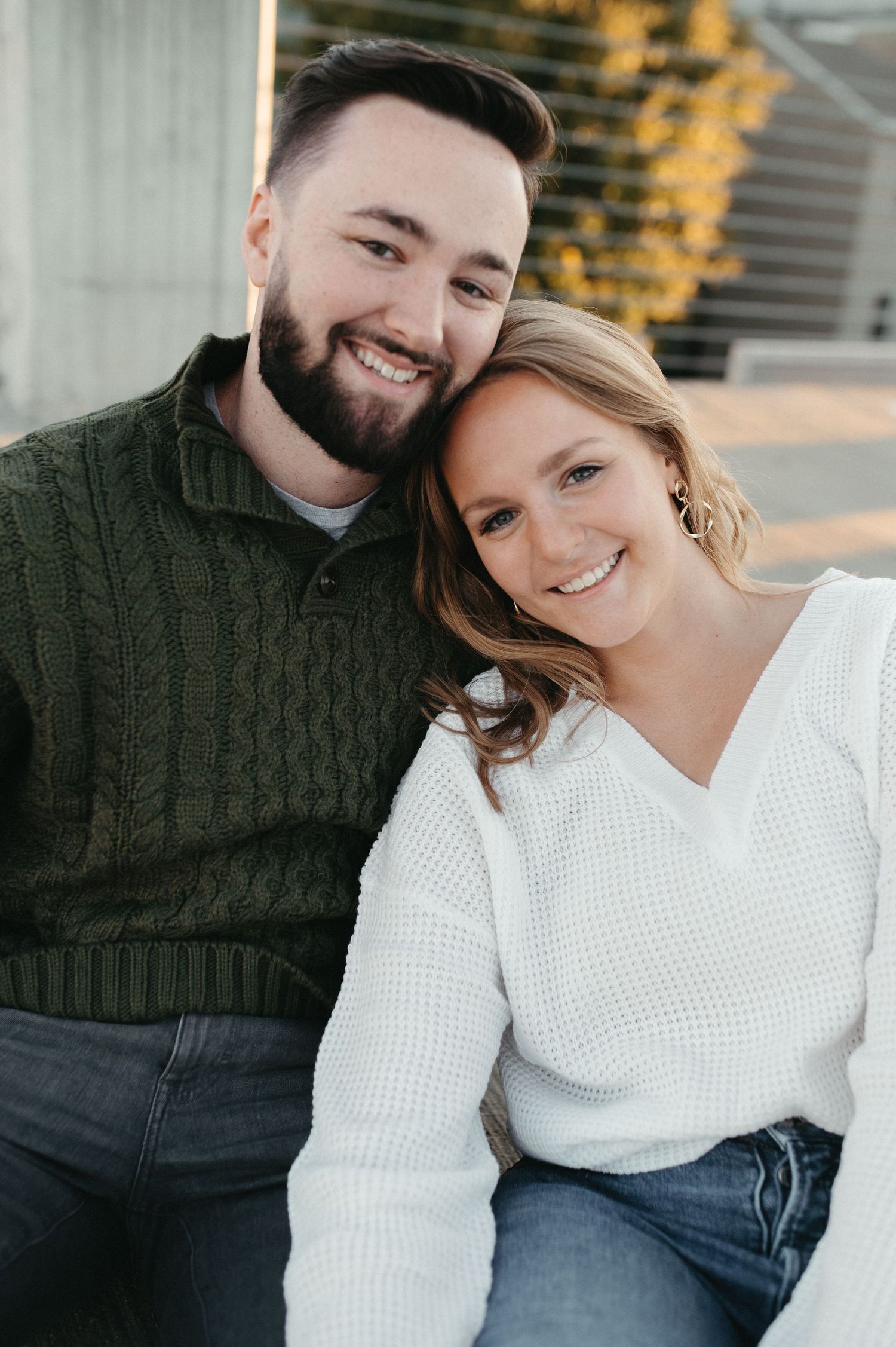 A cozy couple in matching sweaters smile warmly while posing together outdoors.