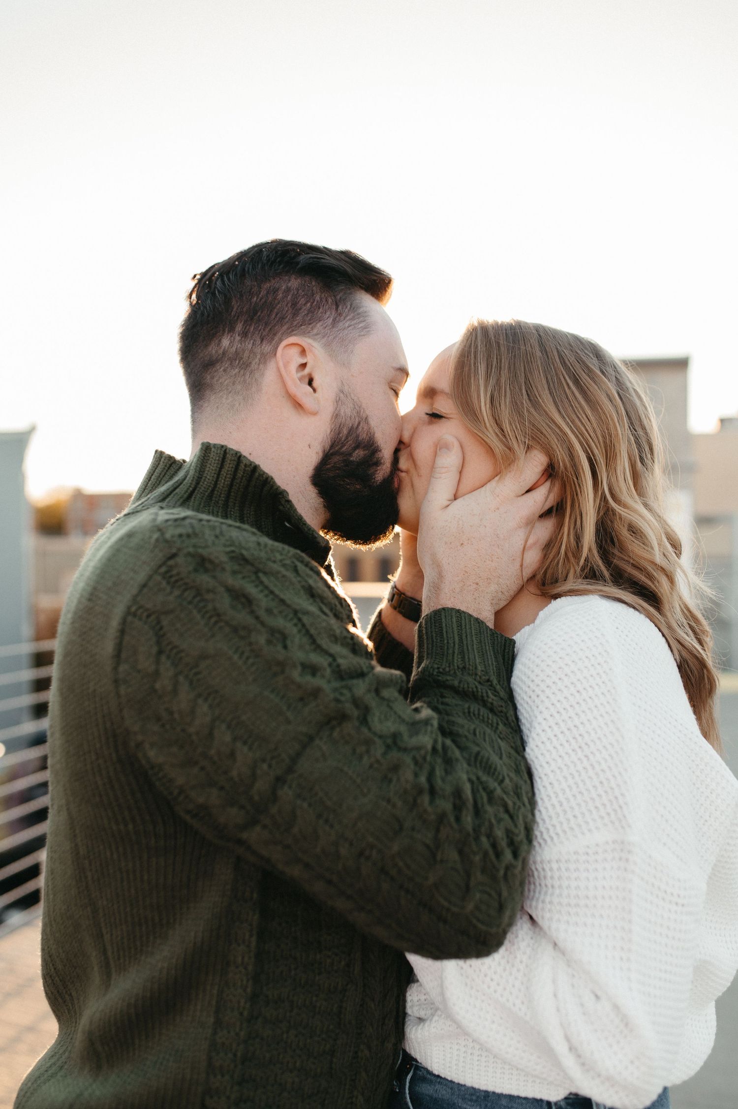 Romantic kiss captured during rooftop engagement session at sunset.