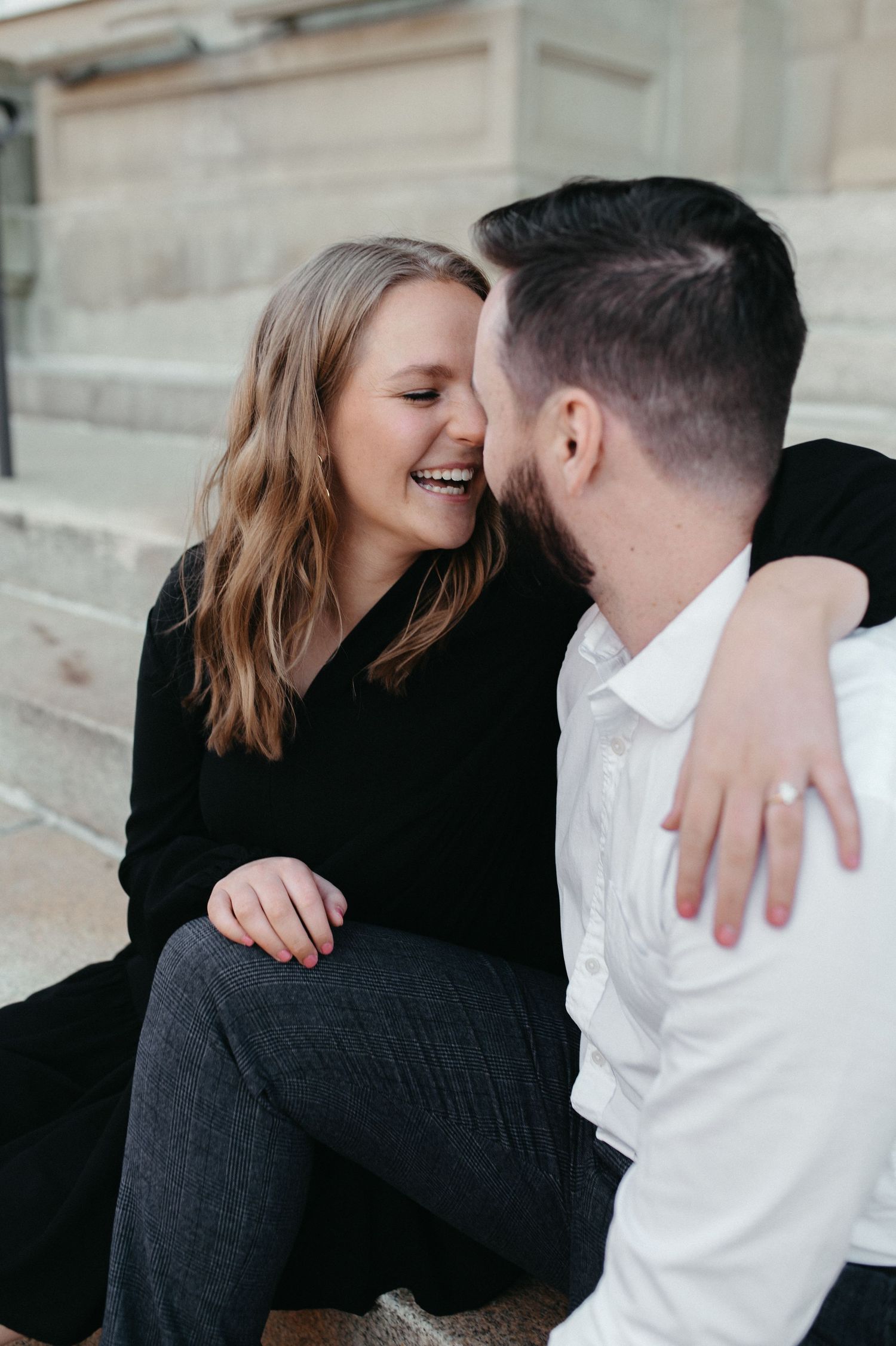 Joyful couple embracing and laughing while seated on stone steps.