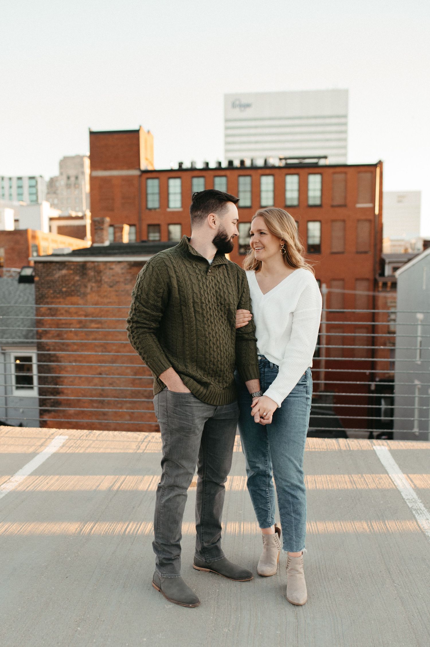 A couple shares a romantic moment on an urban rooftop with brick buildings in the background.
