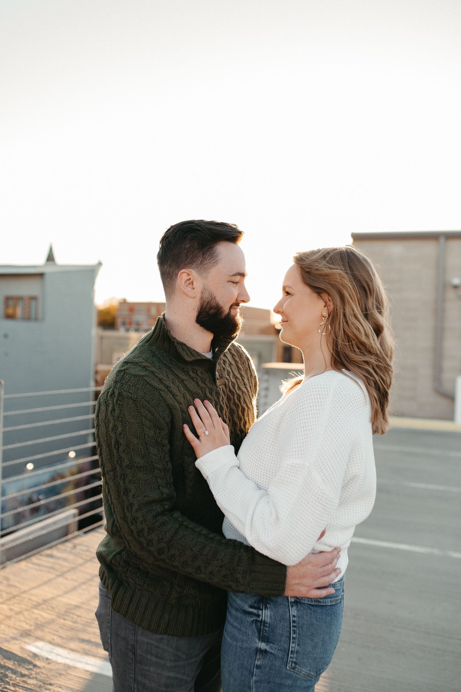 A tender moment between a couple in warm sweaters on an urban rooftop.