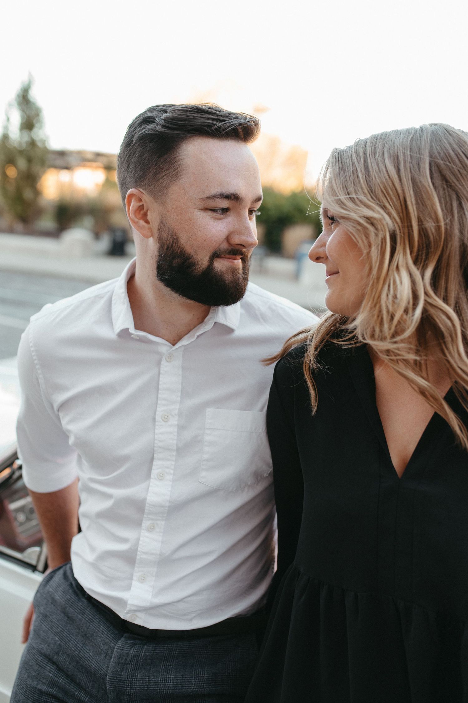 A romantic moment captured between a couple in casual formal attire during sunset.