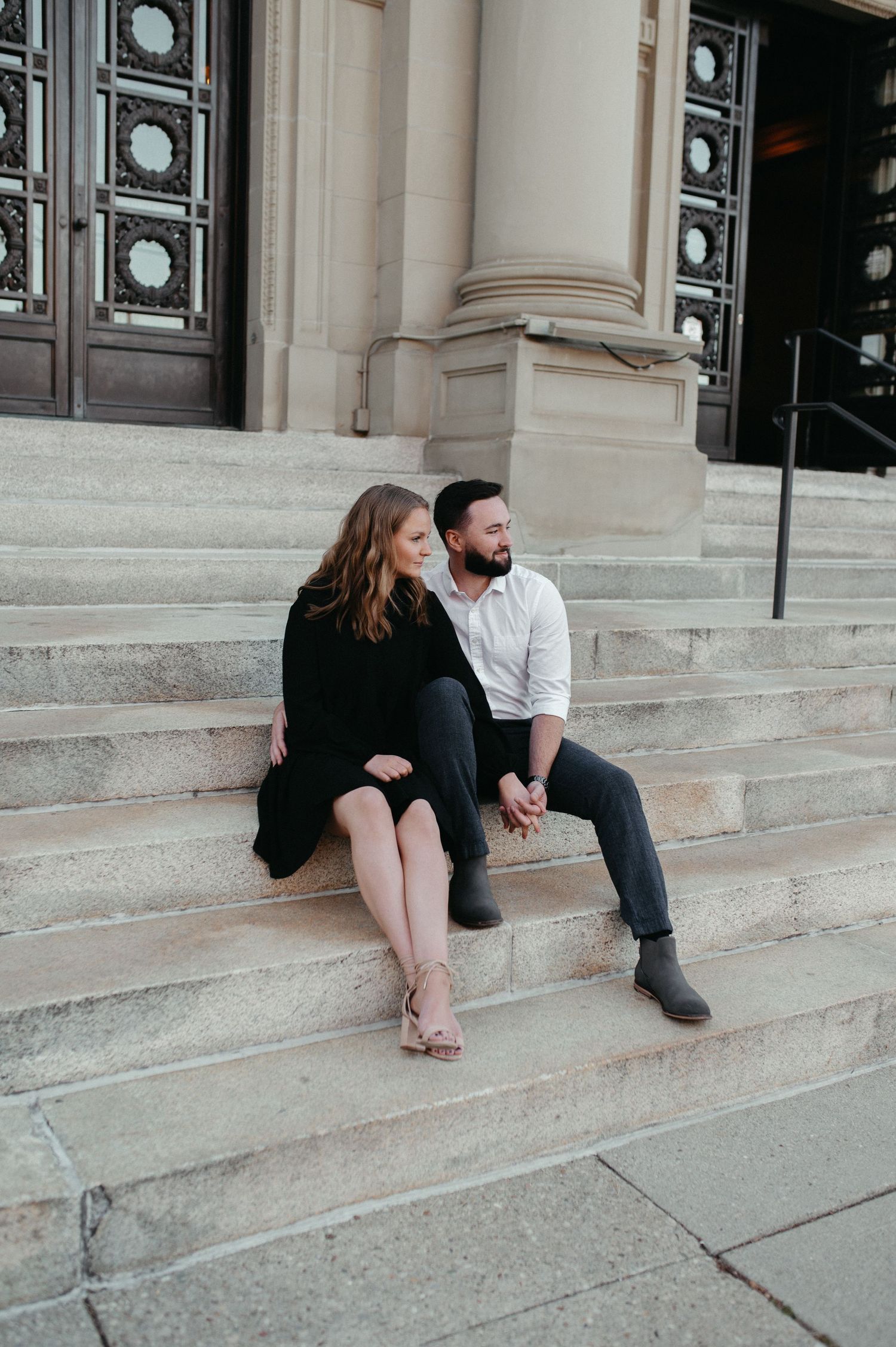 A couple poses on grand stone steps in front of an architectural entrance during their photoshoot.