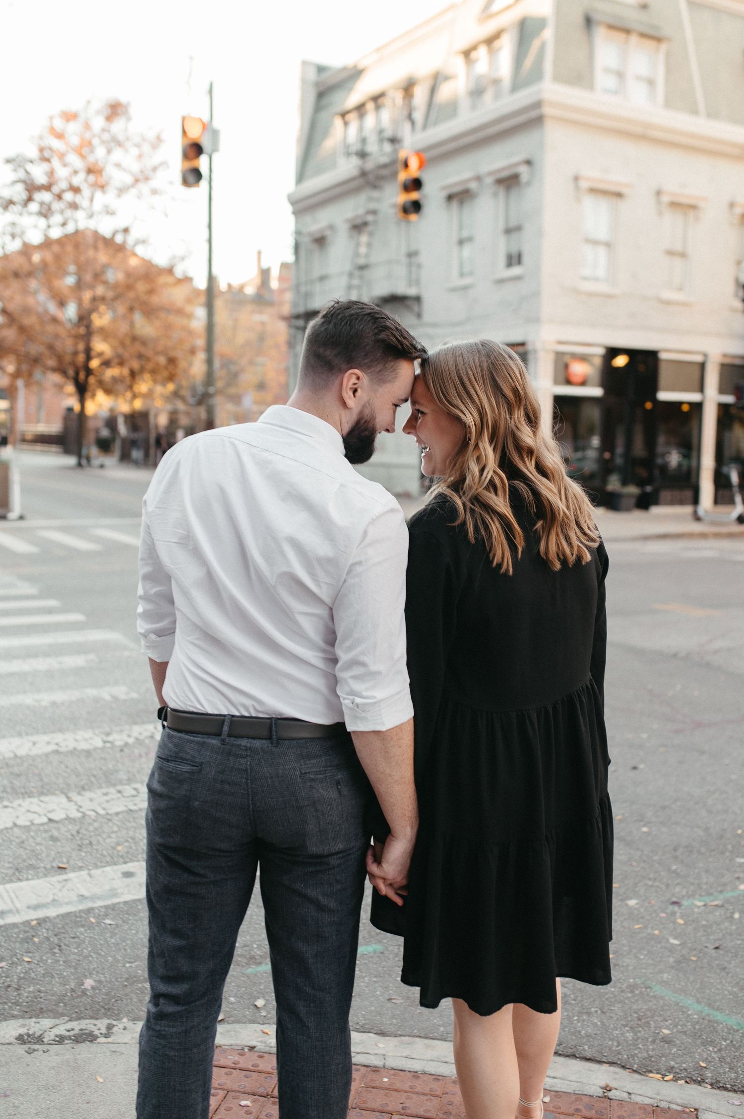 A couple leans in close together while standing at an urban intersection.