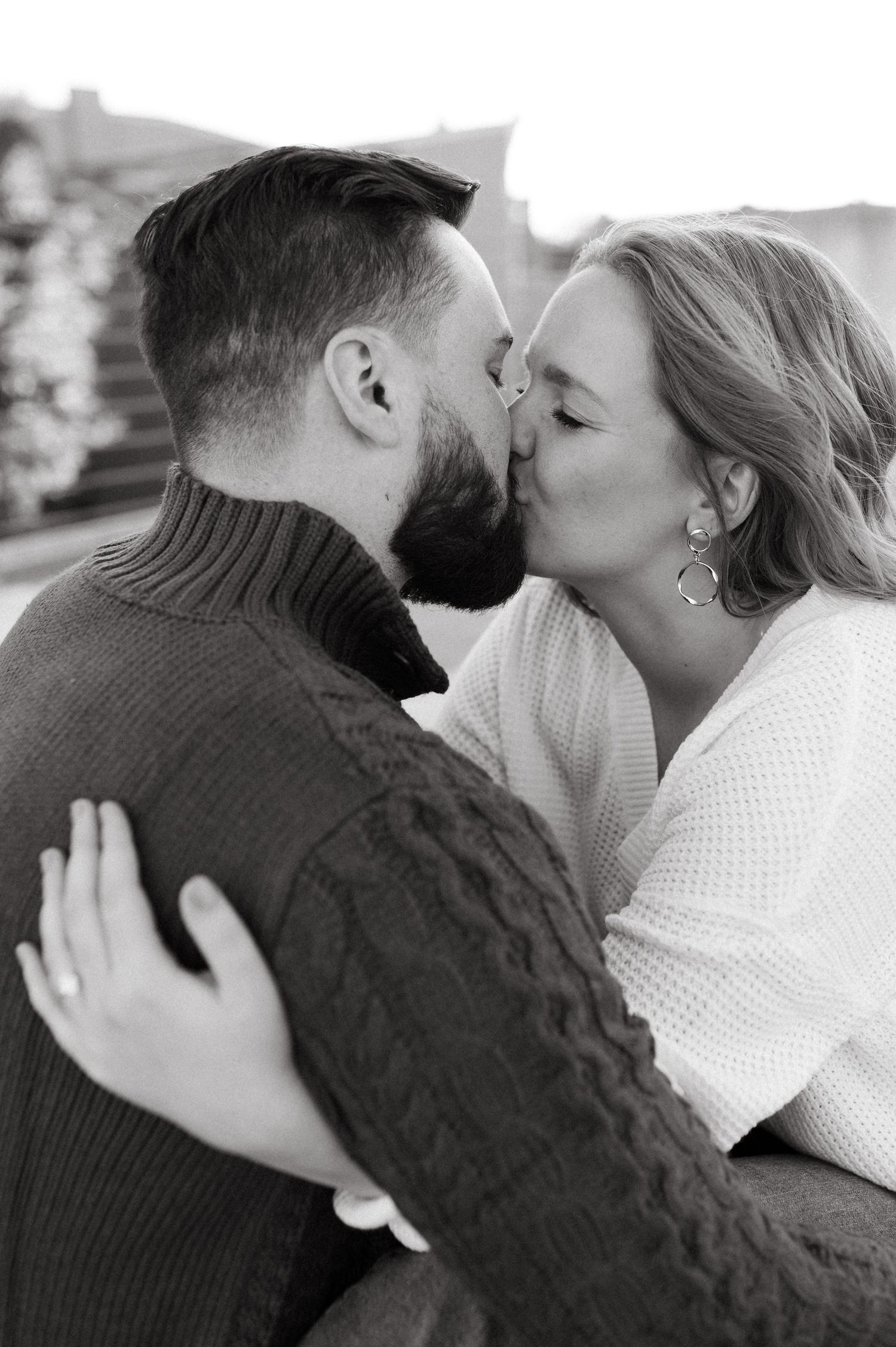 Black and white portrait of an intimate kiss between a couple in knit sweaters.