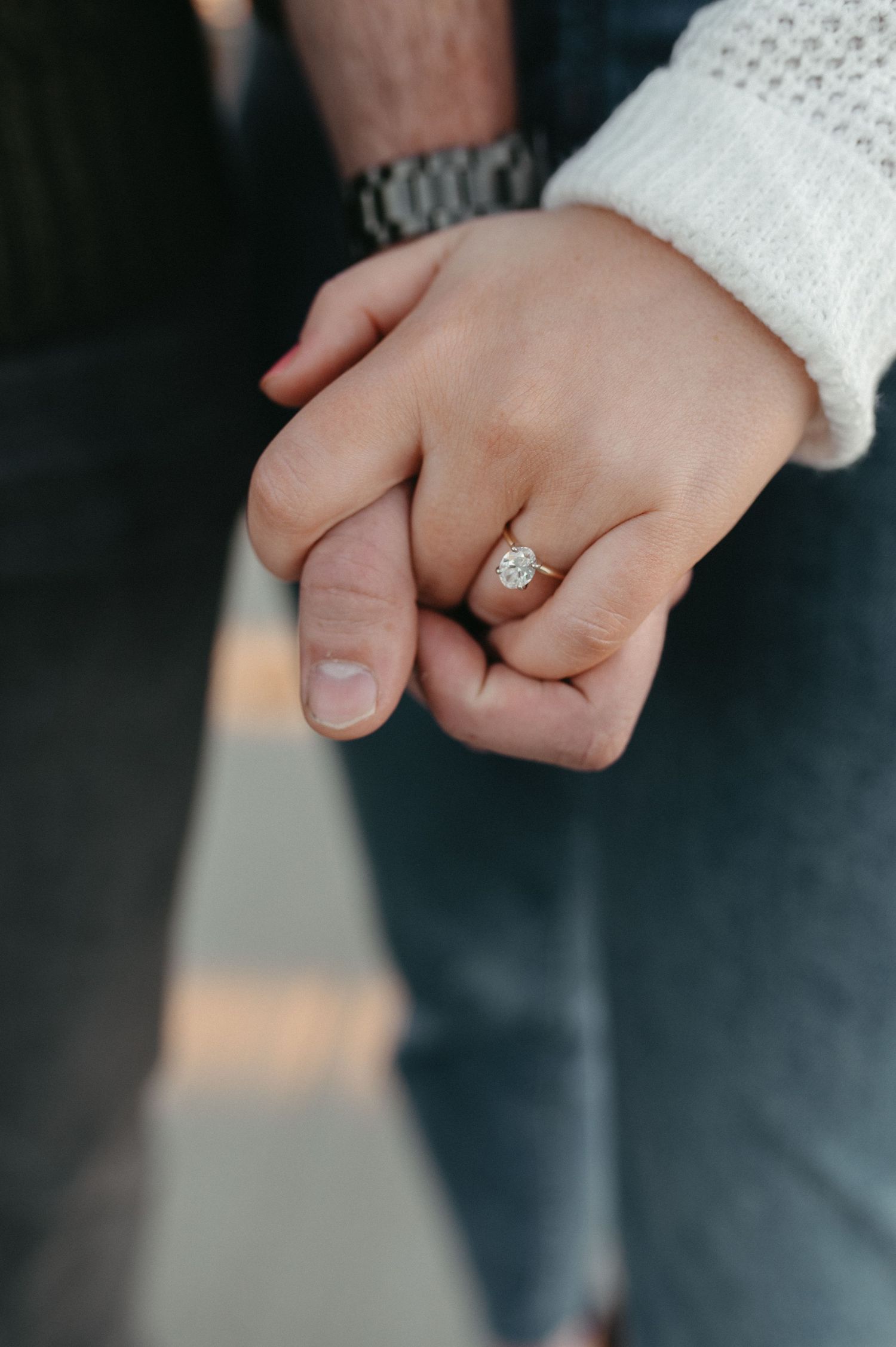 Close-up detail of intertwined hands displaying a sparkling engagement ring.