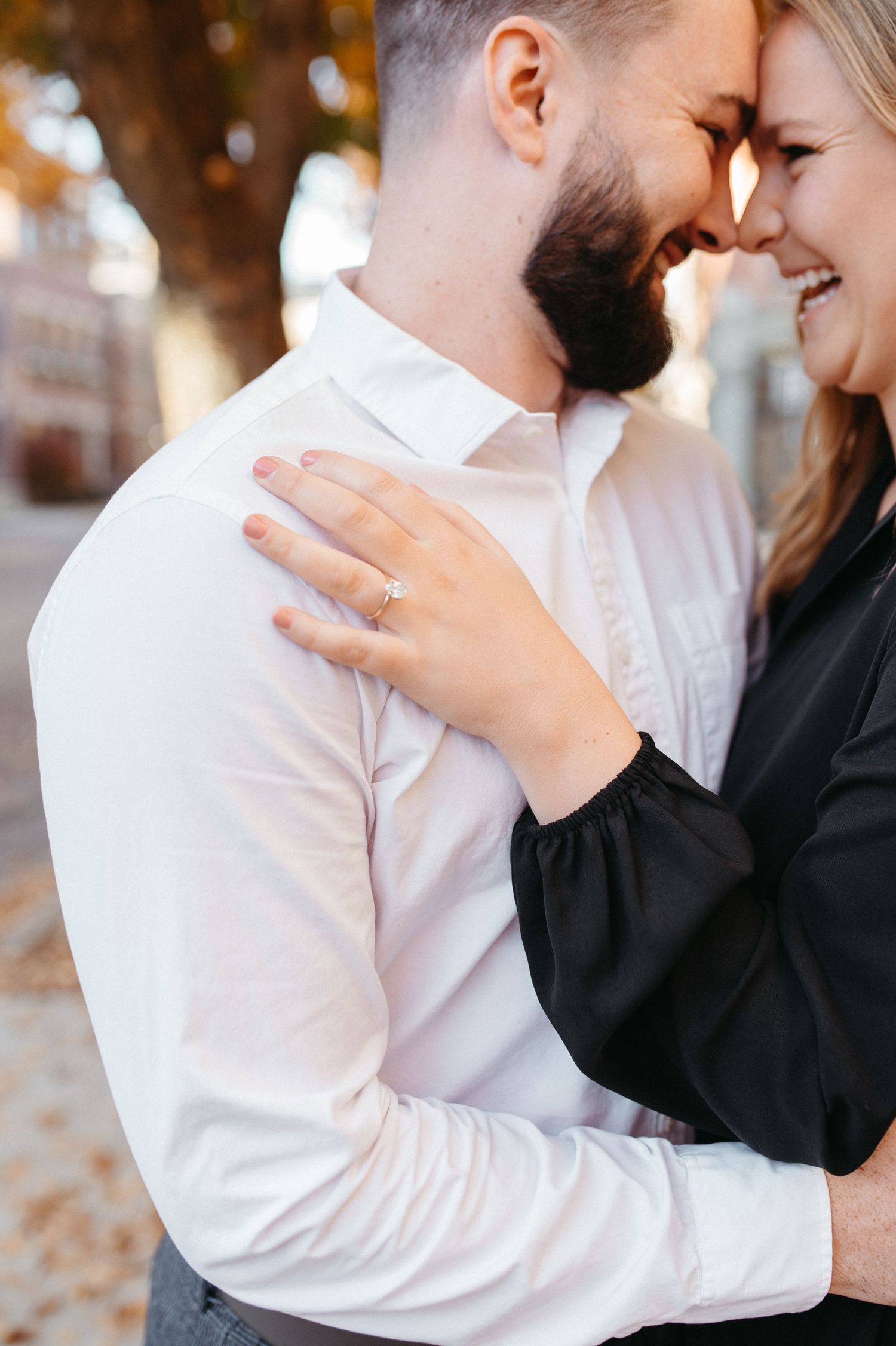 Joyful couple embracing on an autumn sidewalk with golden trees in the background.