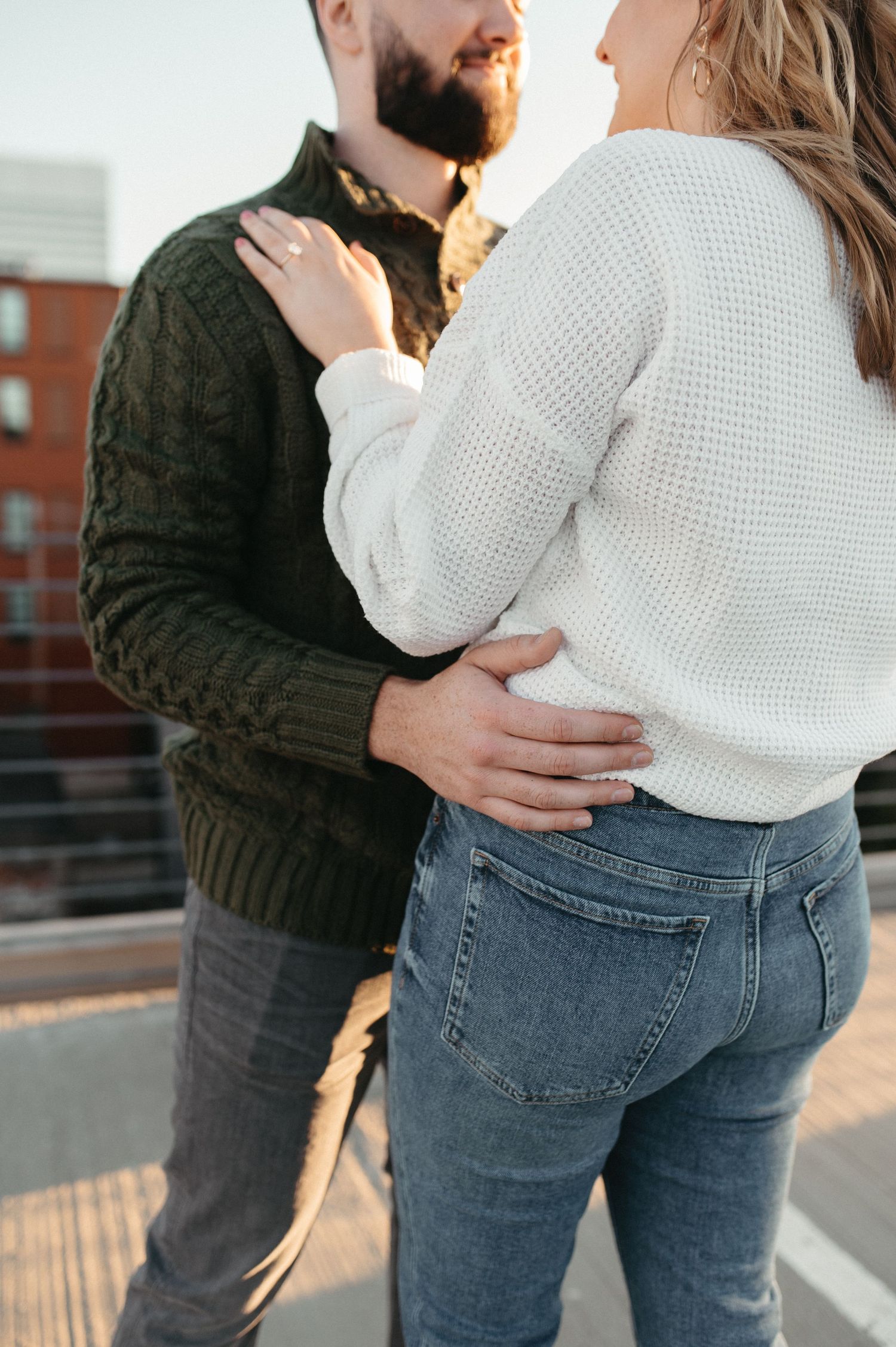 Close-up of couple embracing in contrasting sweaters during outdoor photoshoot.