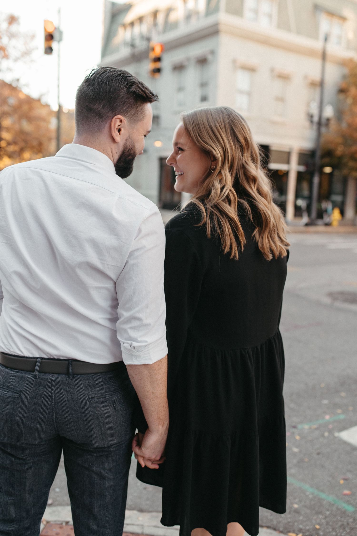 Couple sharing intimate moment on city street with autumn trees in background.