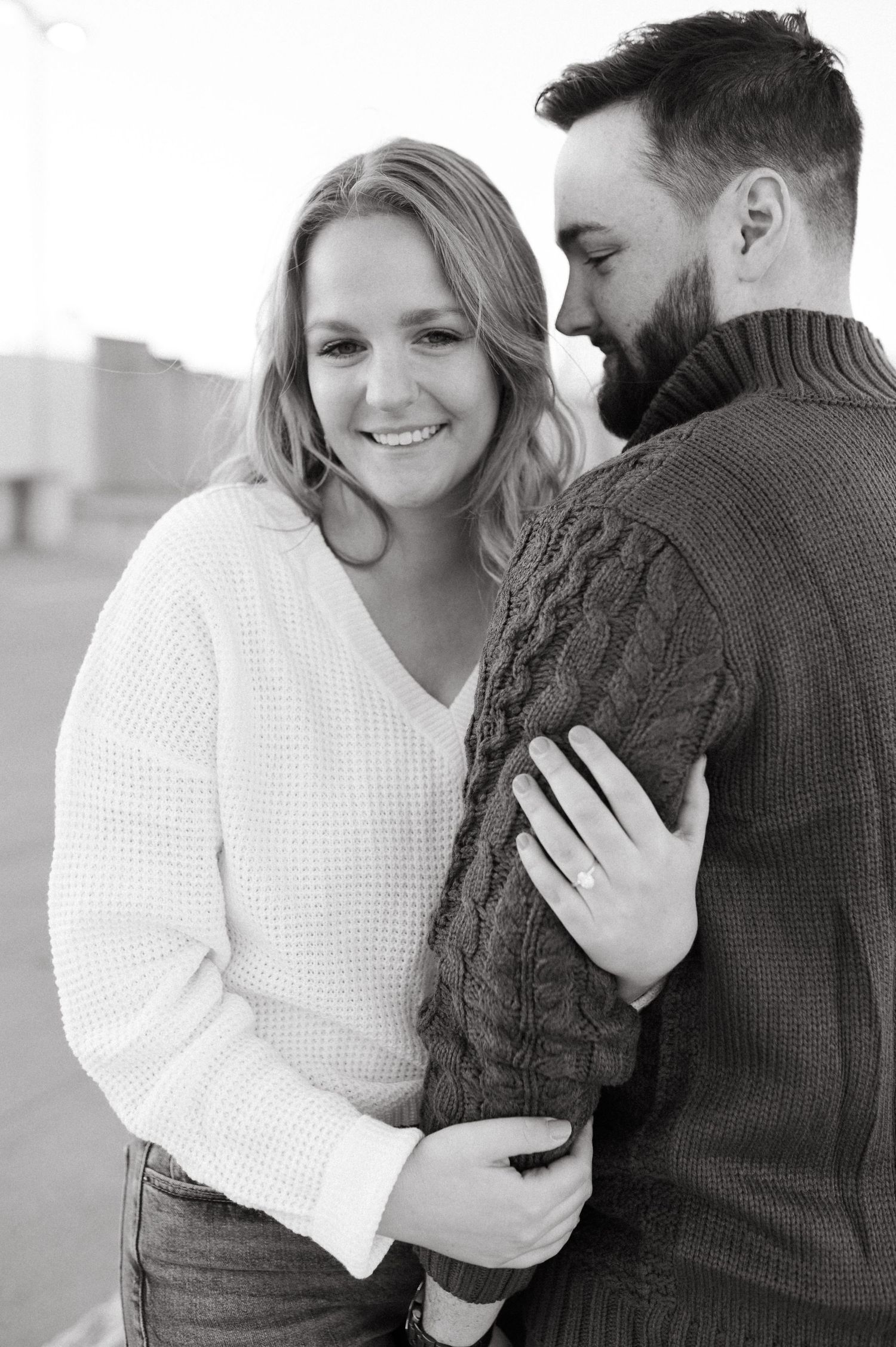 Black and white portrait of a couple sharing a joyful moment in matching sweaters.