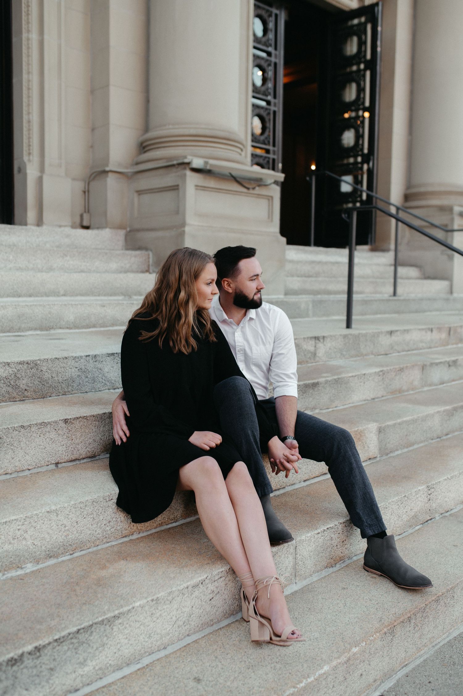 A couple sitting intimately on stone steps in front of a classic building entrance.