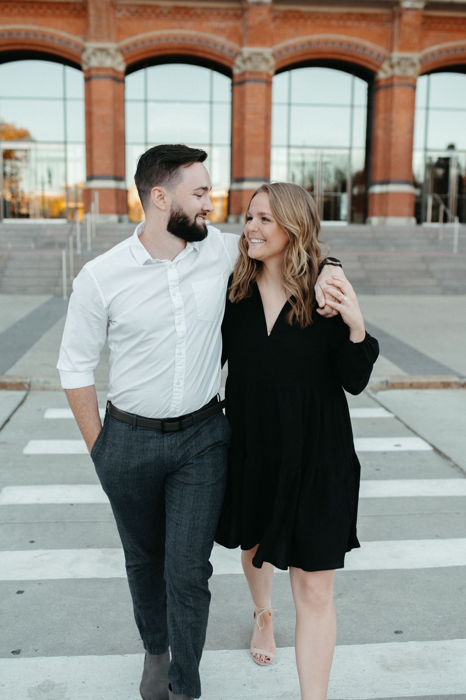A couple shares a loving moment in front of a historic brick building with arched windows.