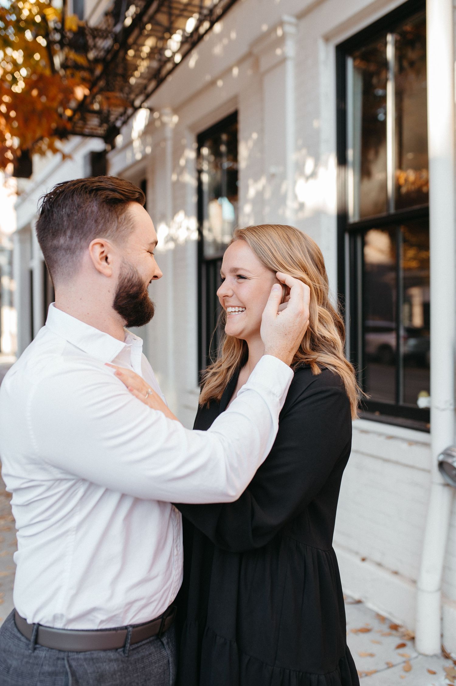 A romantic moment between a couple on a city street with autumn trees and a white building facade.