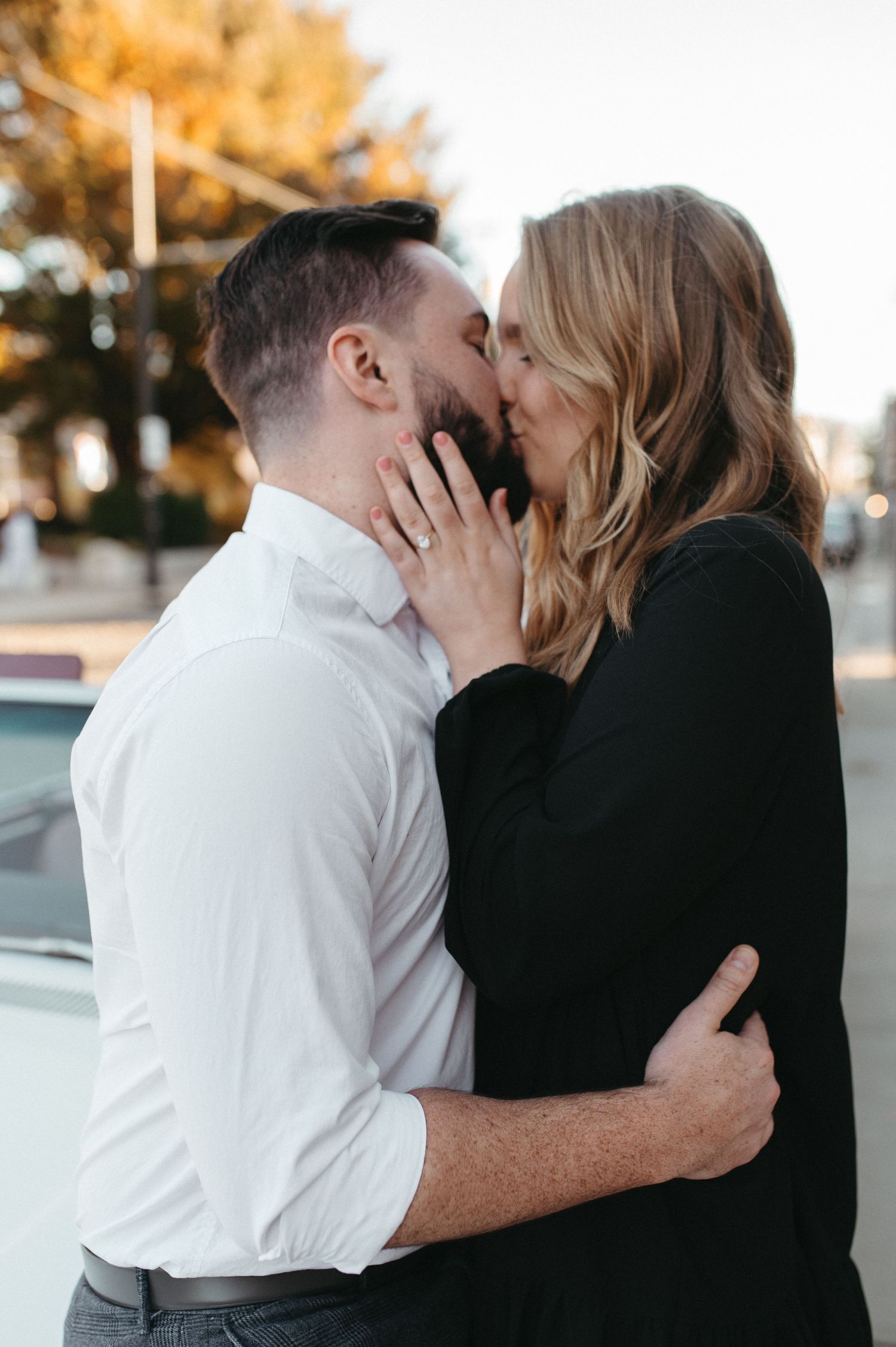A tender moment between a couple sharing a kiss next to a vintage automobile.