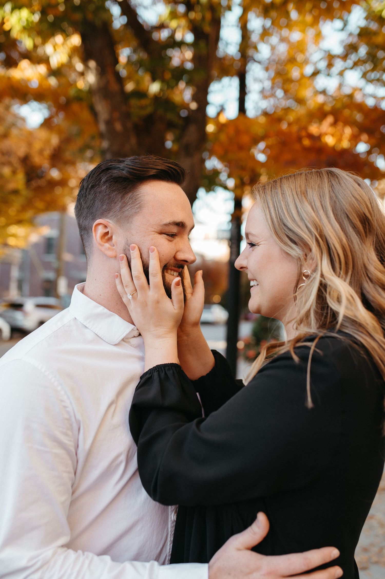 Romantic couple sharing a tender moment on a leaf-covered city street.