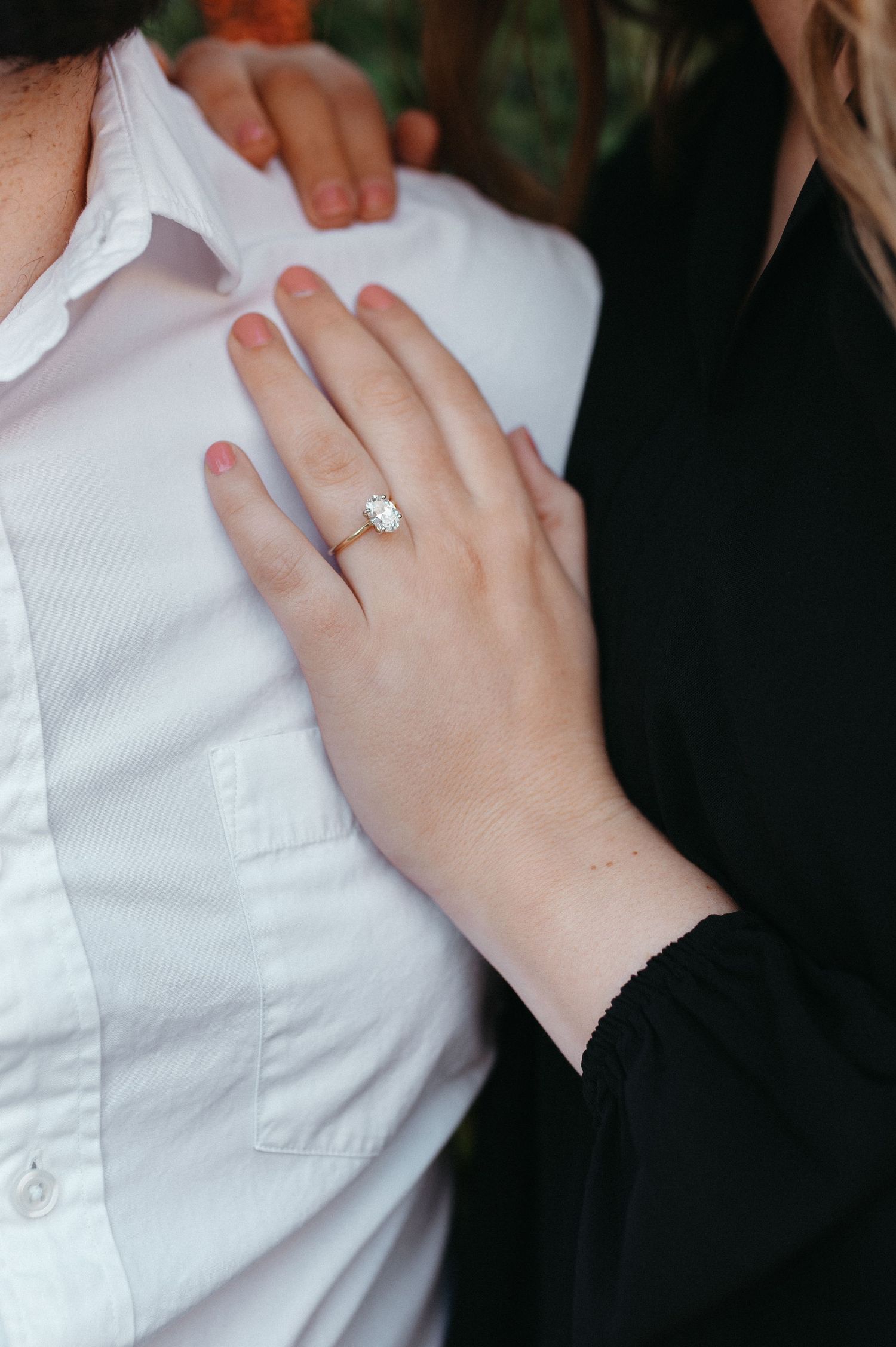 Close-up of an engagement ring on a hand resting against a white dress shirt.