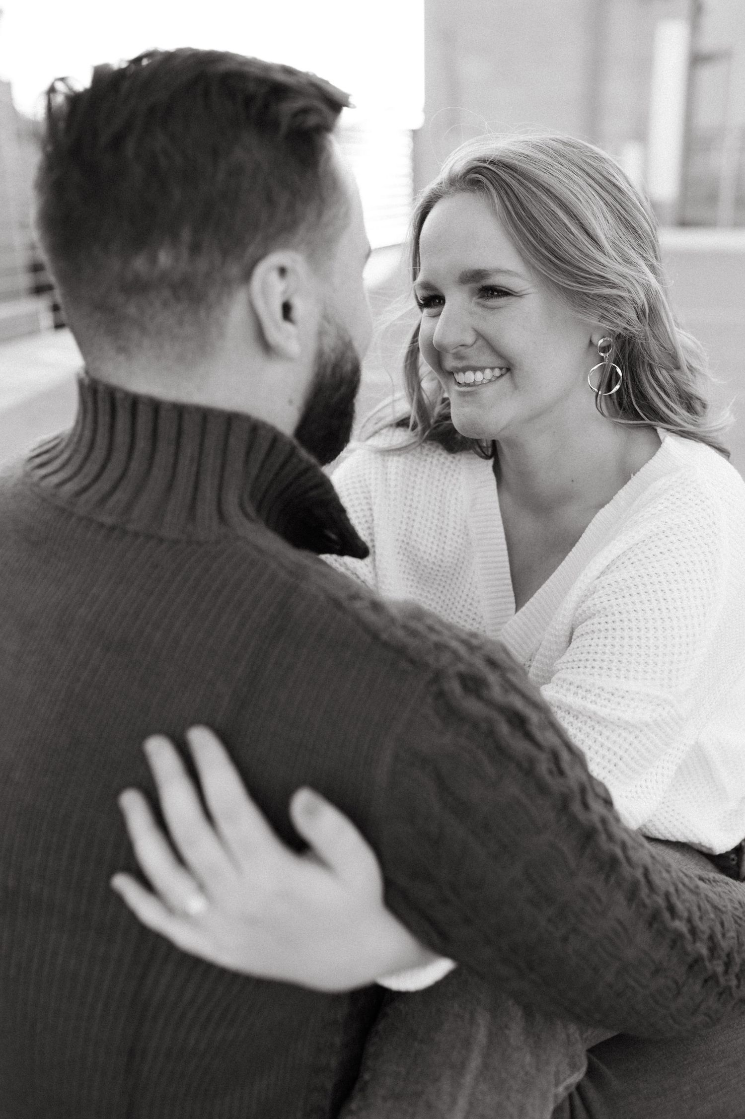 A joyful couple in warm sweaters share a candid laughing moment during their photoshoot.