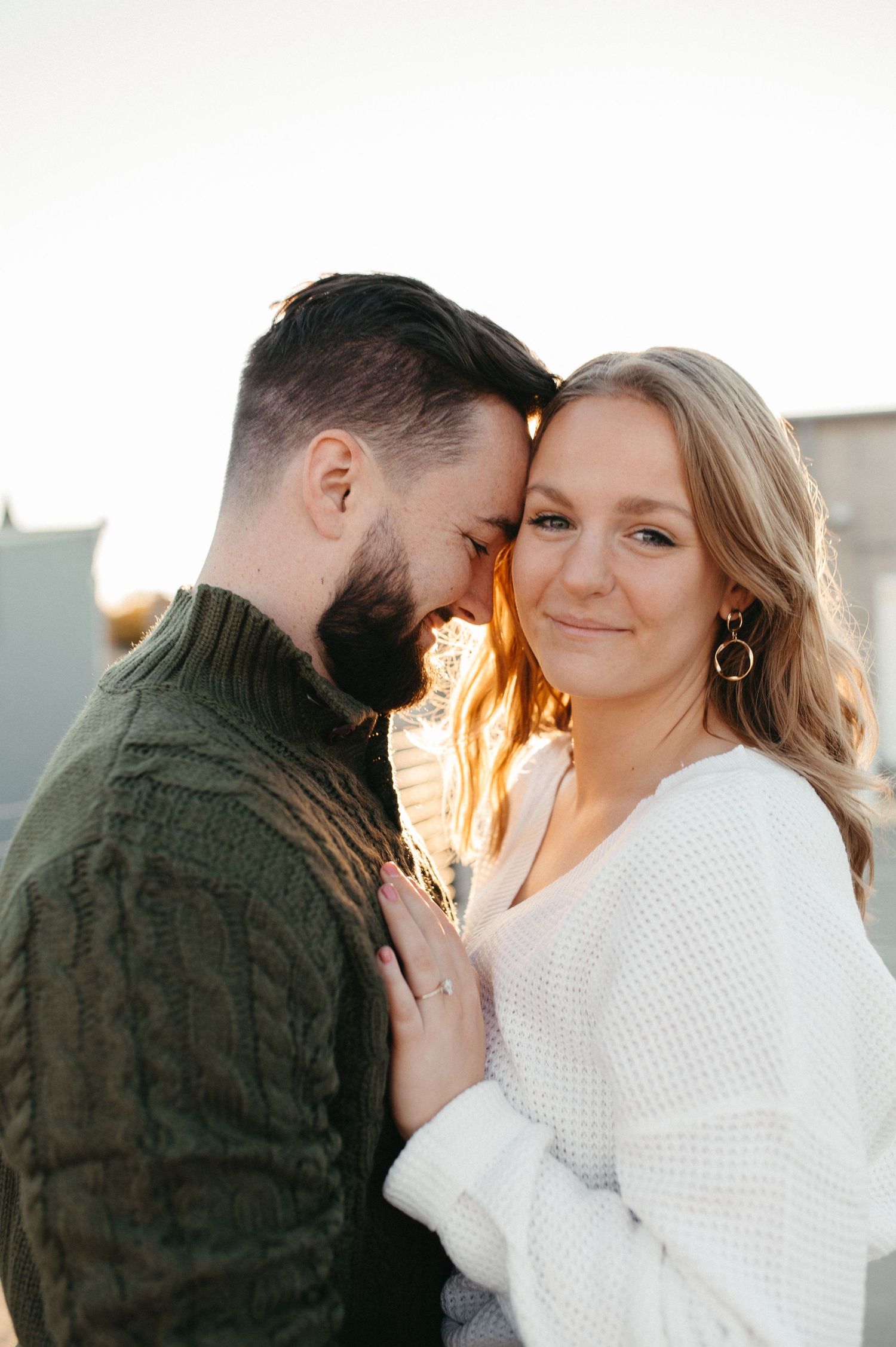 Sweet moment between couple in contrasting sweaters during golden hour portrait session.