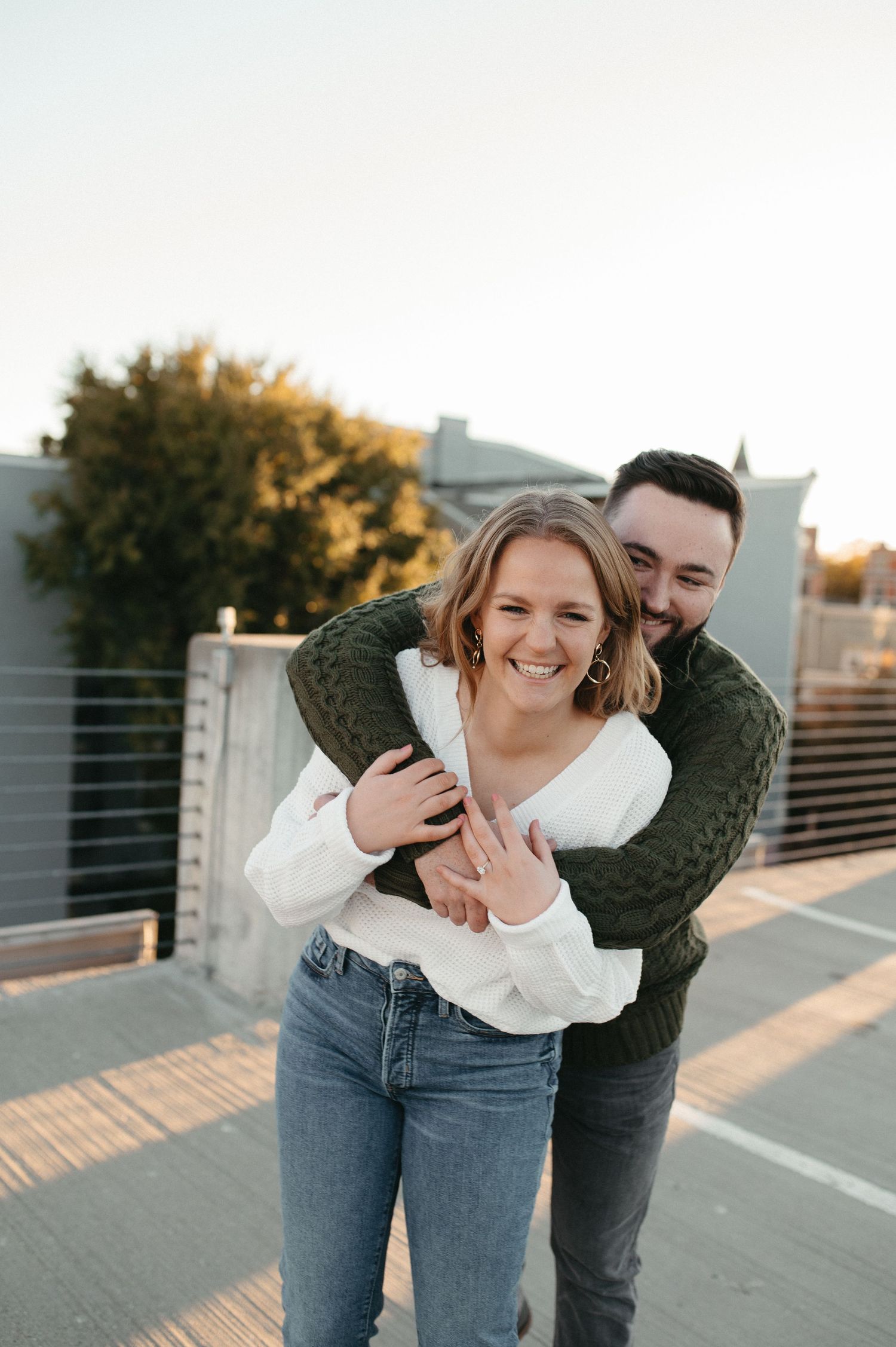 Playful couple laughing during casual rooftop photoshoot at golden hour.