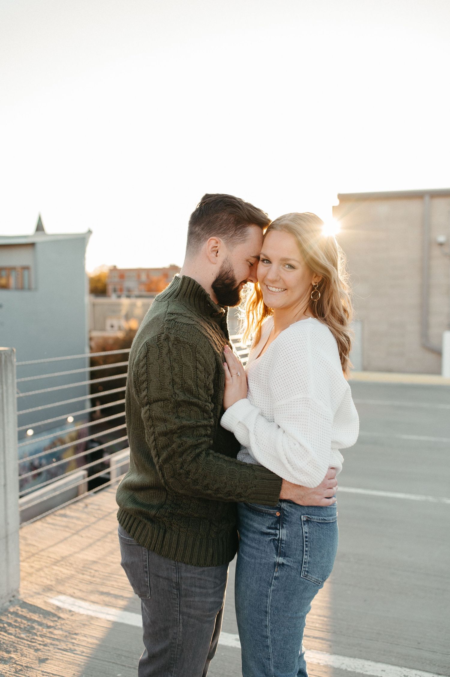 Couple in casual wear embracing on urban rooftop during golden hour photography session.