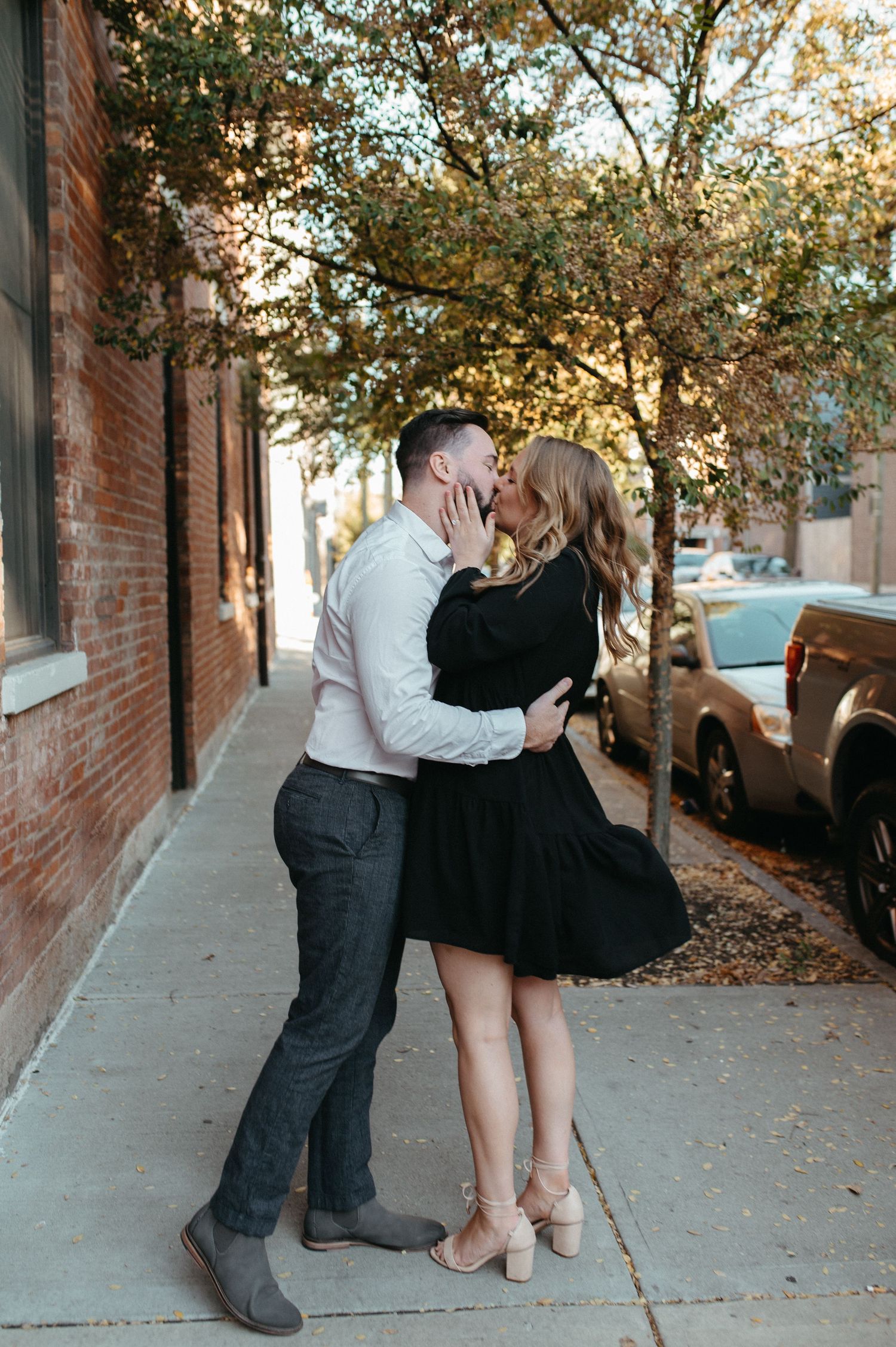 A tender moment between a couple on a tree-lined street with fallen leaves.
