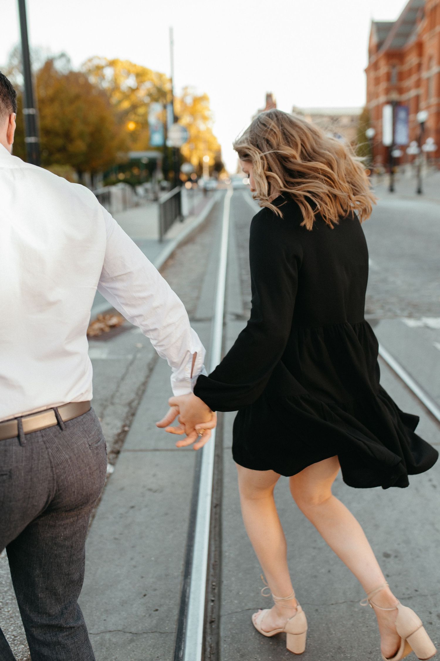 A couple holding hands while walking along trolley tracks during autumn.