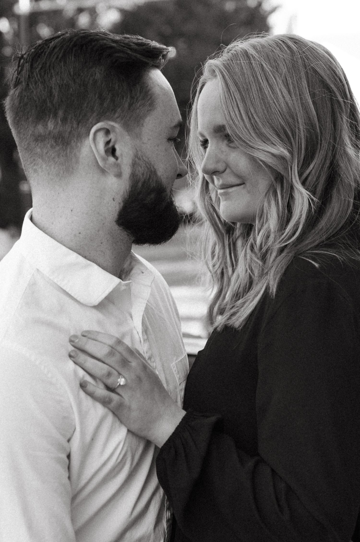 A black and white portrait of a couple sharing an intimate moment near their classic car.