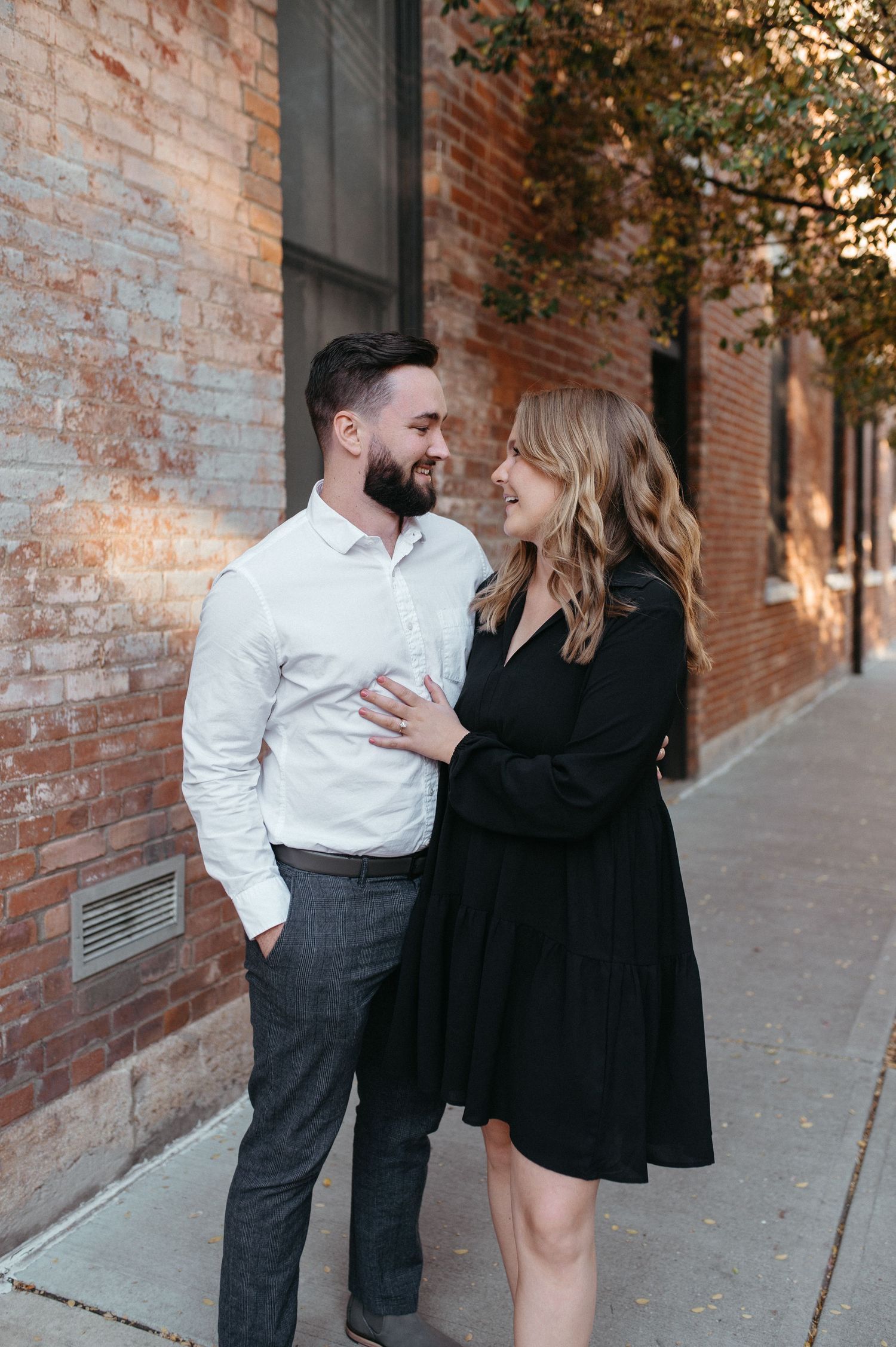 A playful engagement photo of a couple in black and white attire against an urban backdrop.