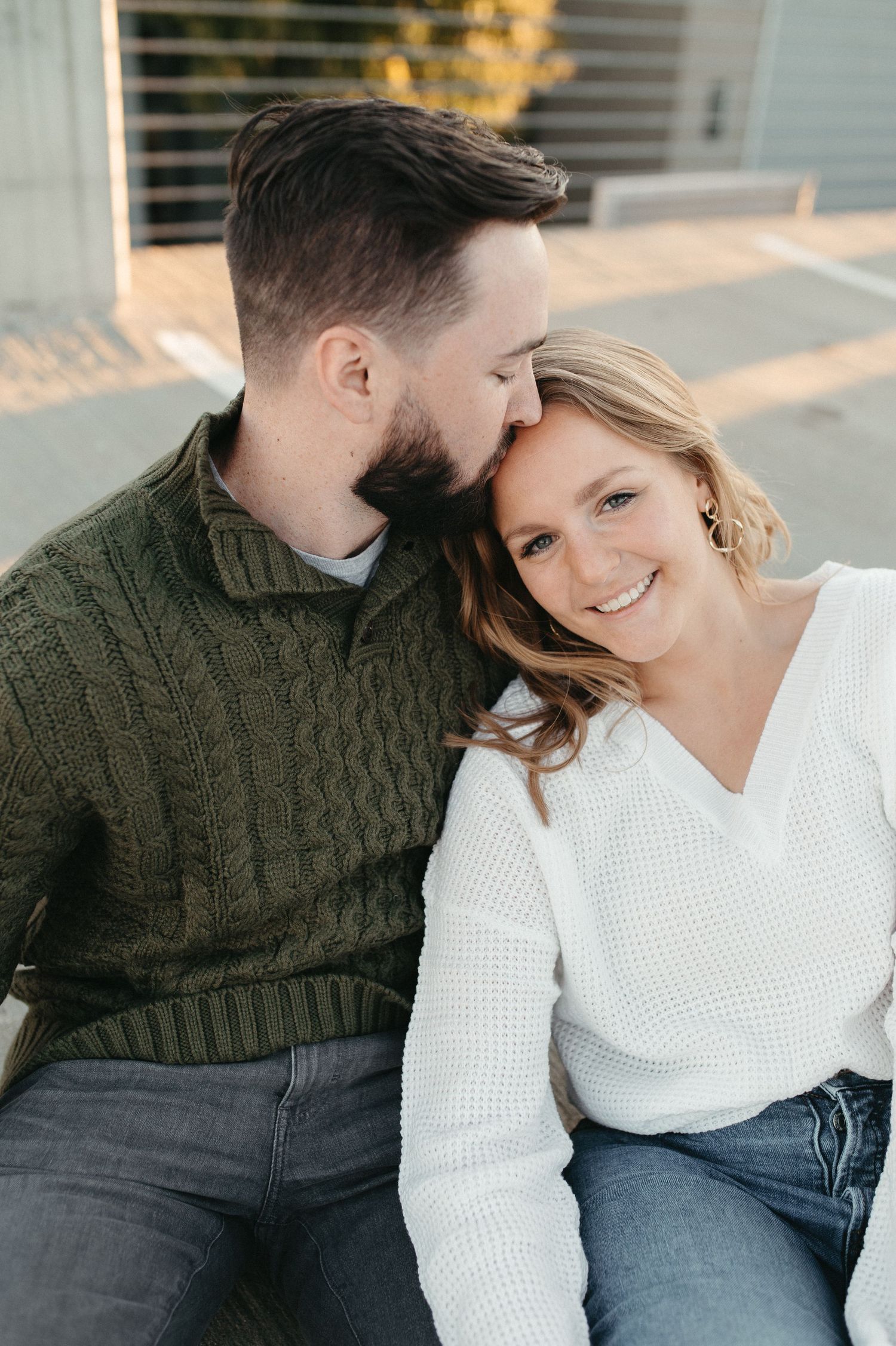 A tender moment between a couple wearing knit sweaters as they sit close together.