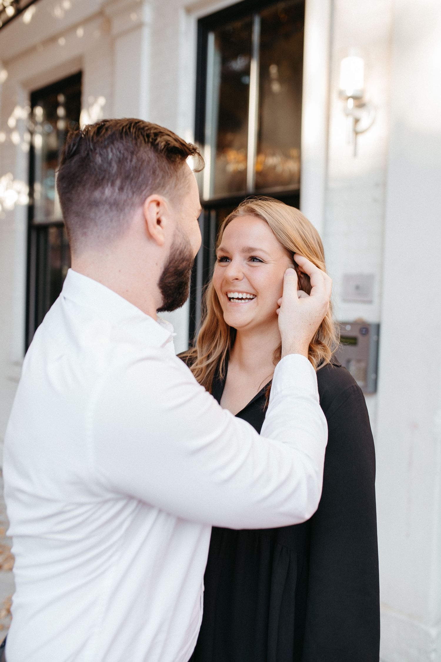 Tender moment between couple outside storefront with white facade.