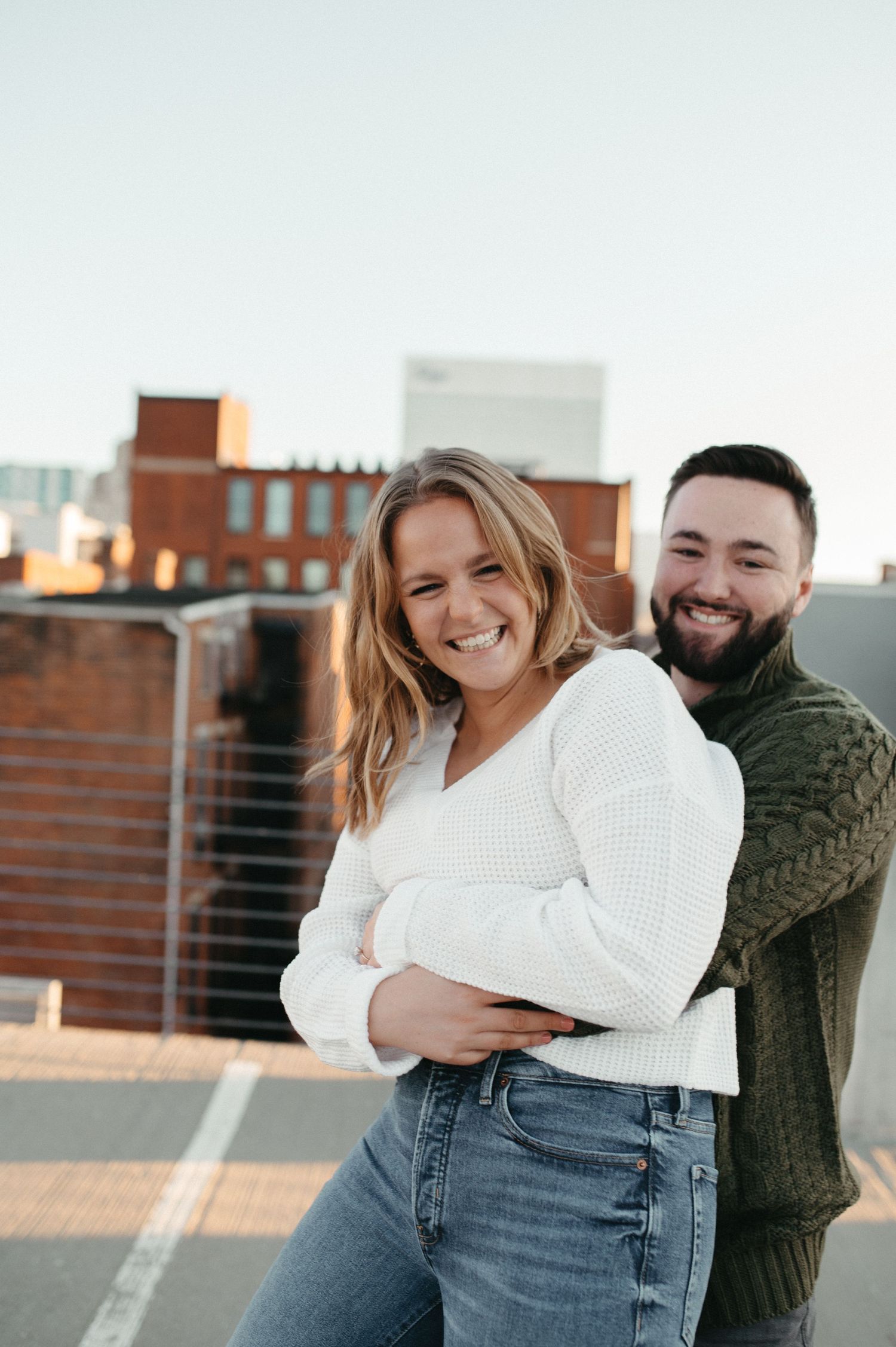 Couple sharing playful moment outdoors with urban backdrop at sunset.